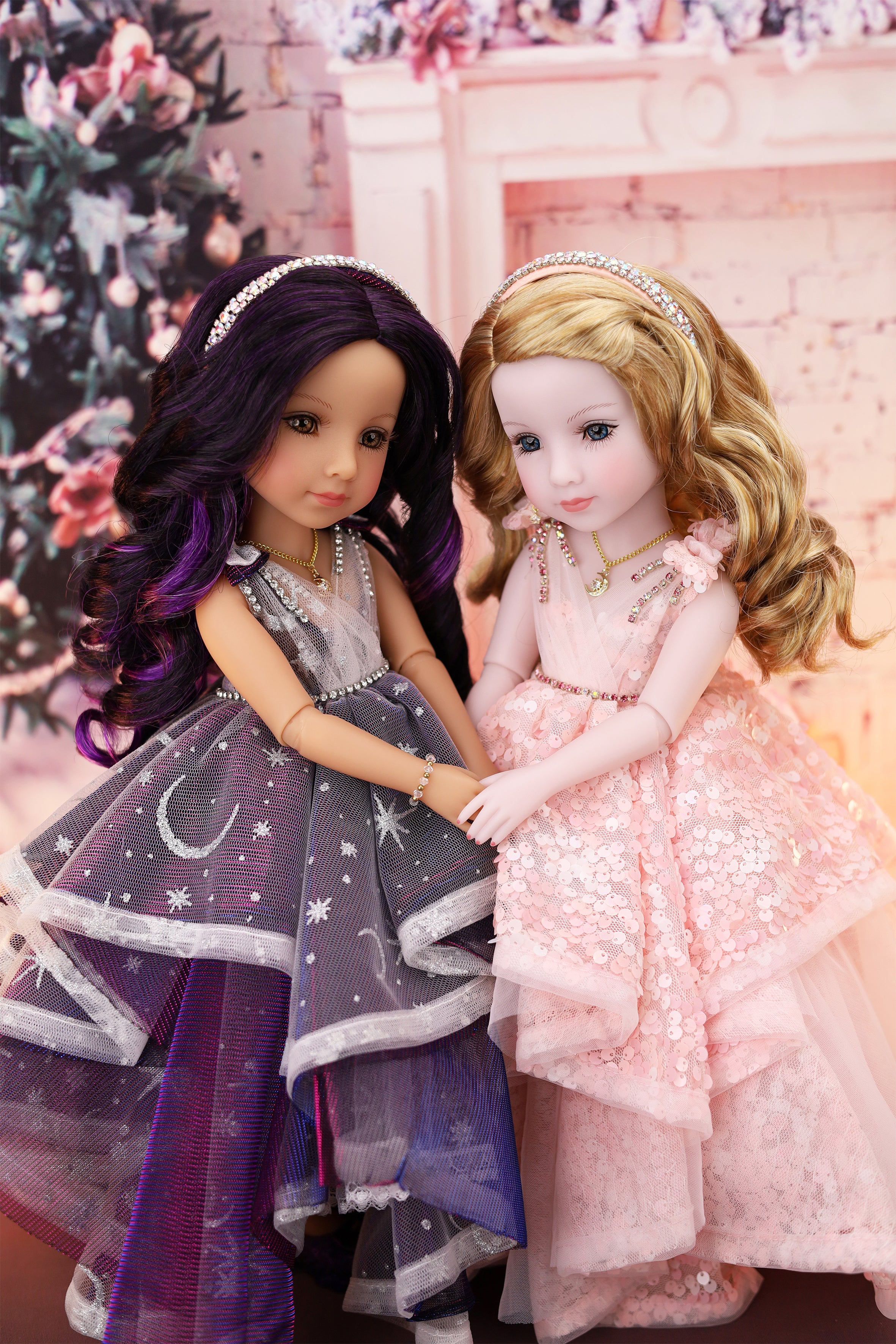 Two dolls in formal dresses standing next to each other with a decorated Christmas tree in the background.
