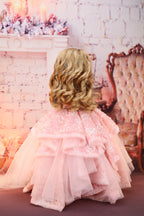 Doll wearing a pink dress with floral embellishments in a vintage-style room.