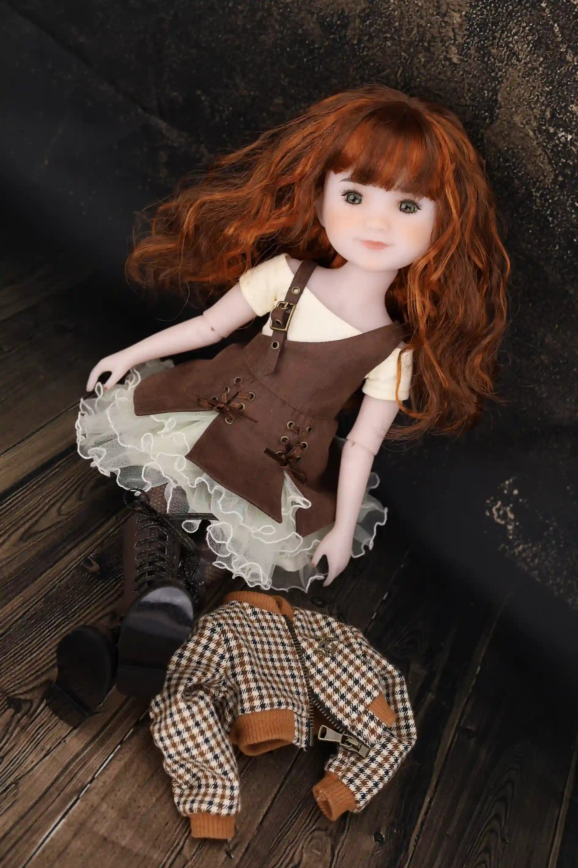 Doll with red hair wearing a brown outfit on a dark wooden floor.