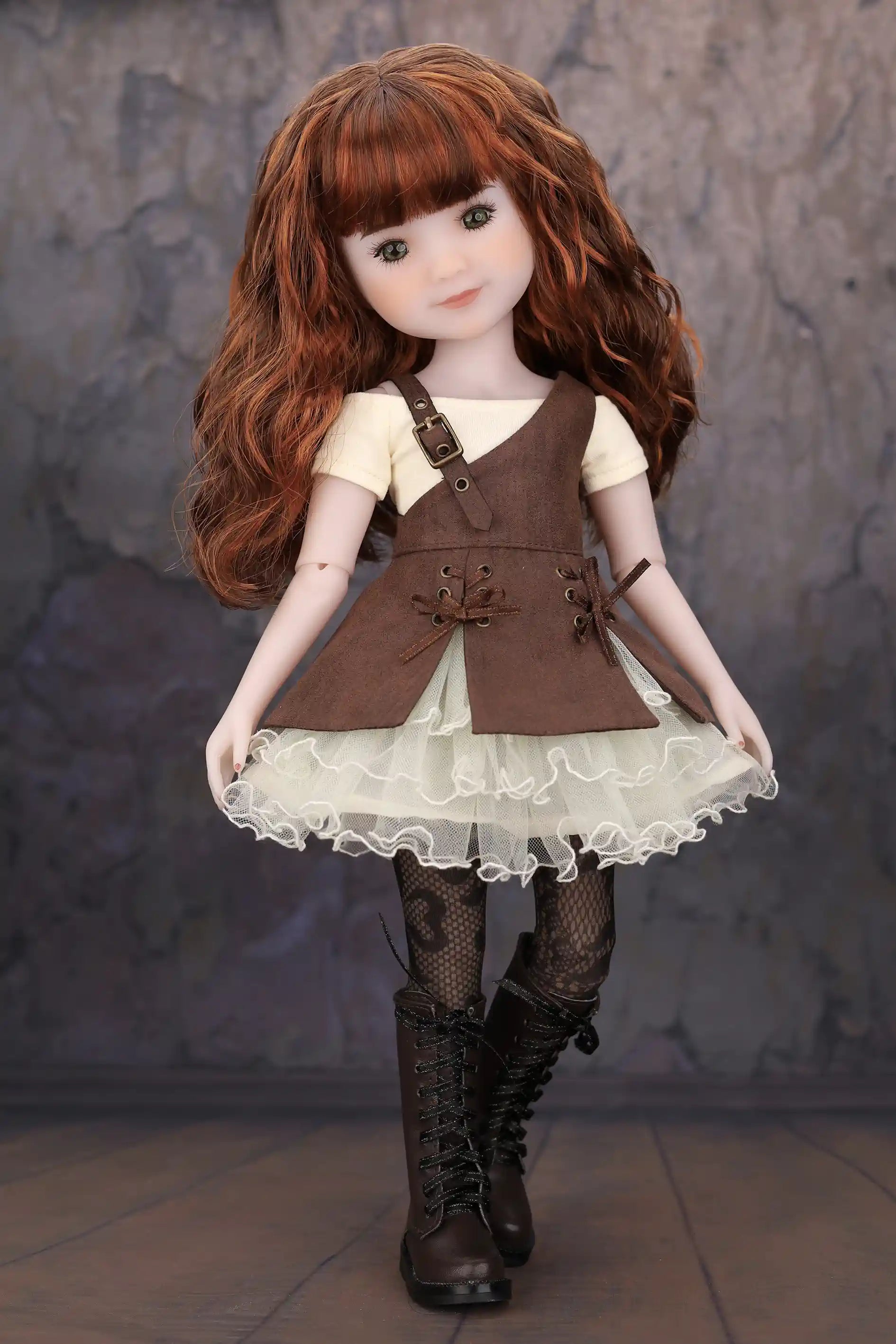 Doll with brown hair wearing a brown dress over a white lace skirt against a textured gray background