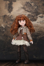 Doll with red hair and a checkered outfit standing against a textured brown background