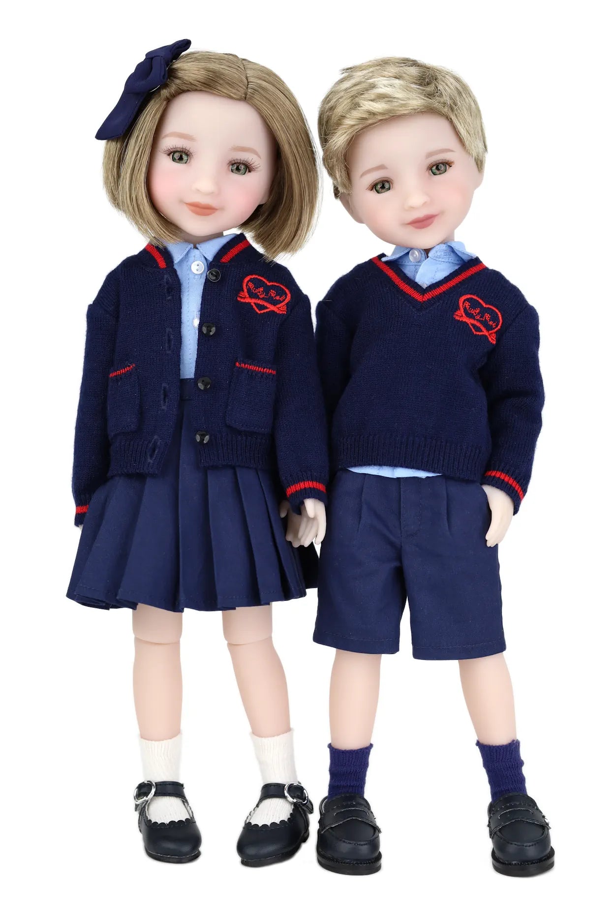 Two dolls in matching school uniforms with navy jackets and shorts on a white background