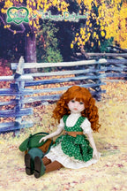 Doll in a green dress sitting on the ground with a wooden fence and trees in the background