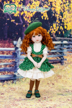Doll in a green dress with a white apron standing in a scenic outdoor setting.