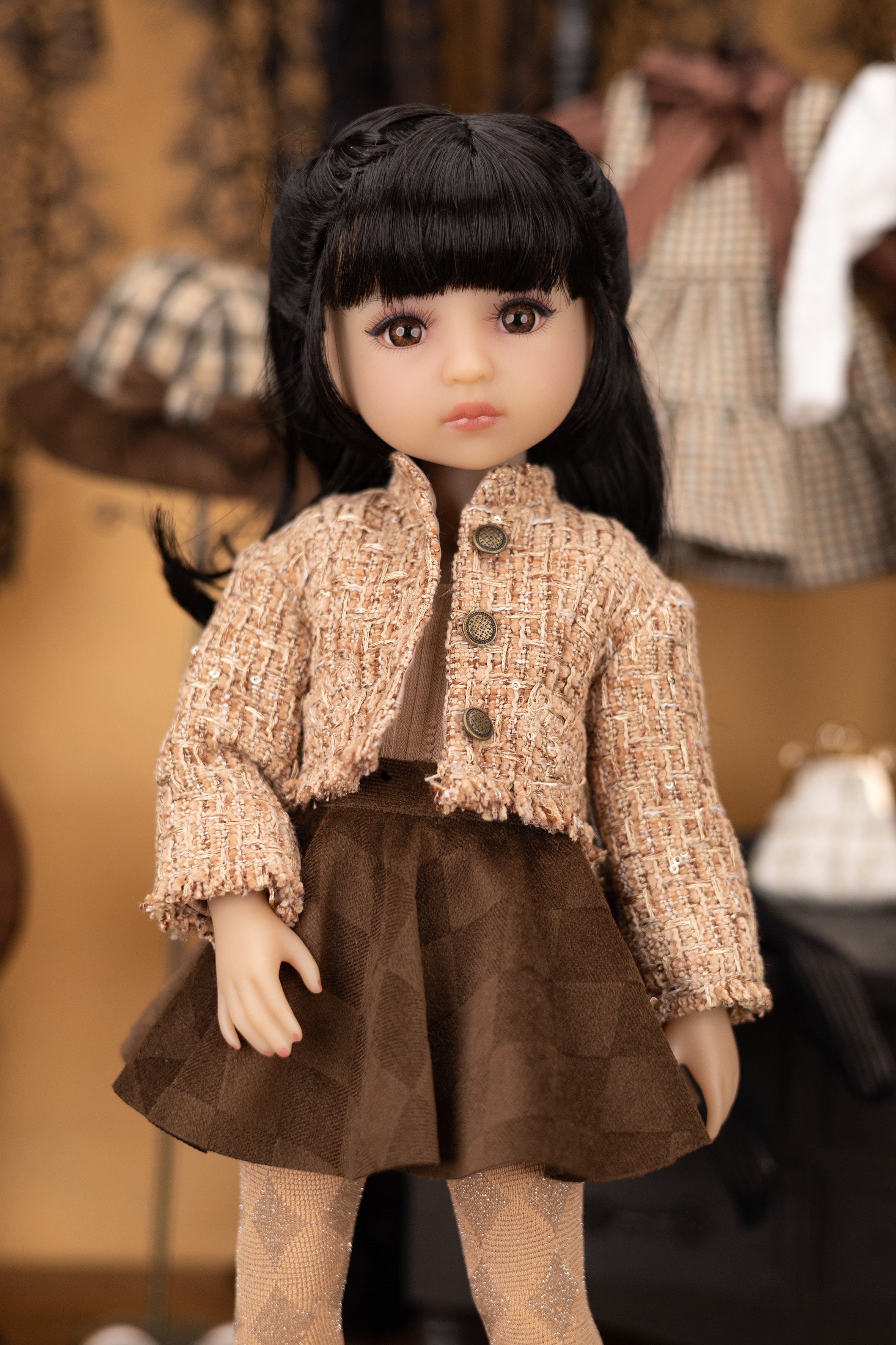 Doll wearing a tweed jacket and brown skirt in a blurred indoor setting