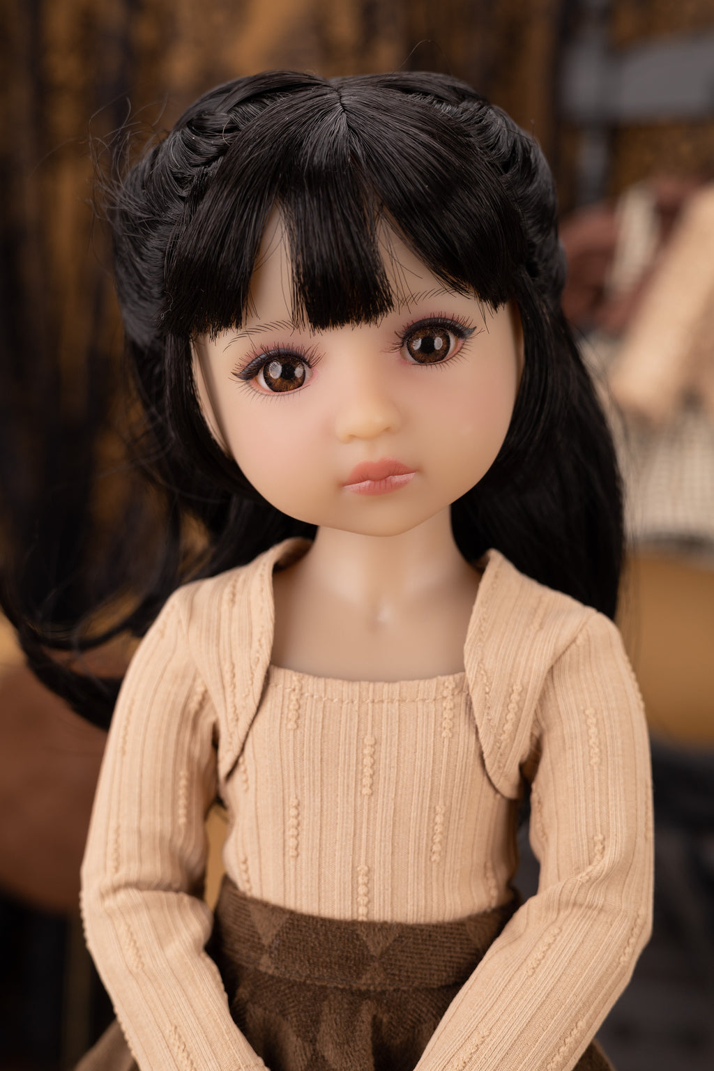 Doll with black hair and a beige outfit against a blurred background