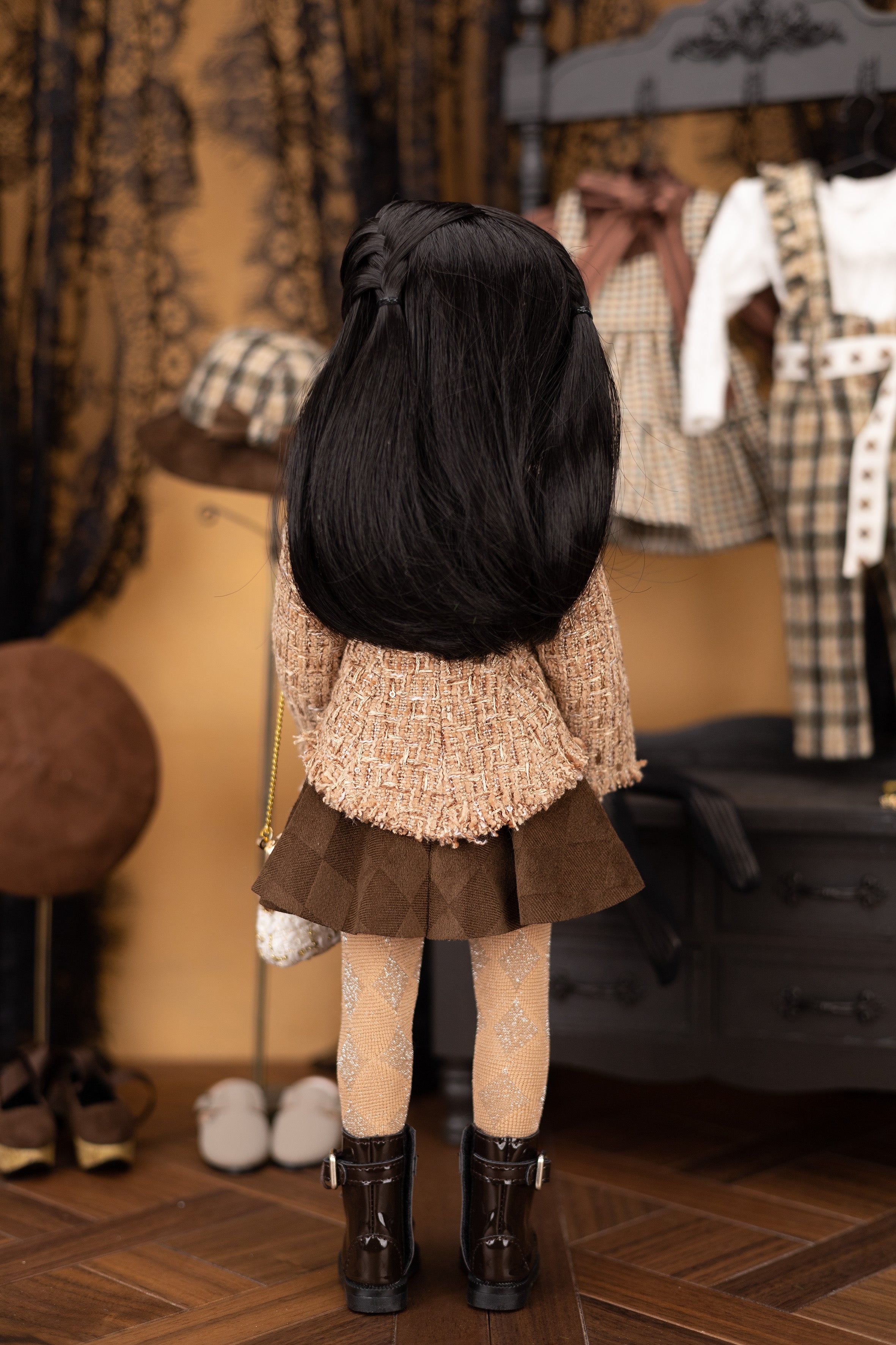 Doll wearing a textured beige jacket and brown skirt in a room with mannequins and clothing.