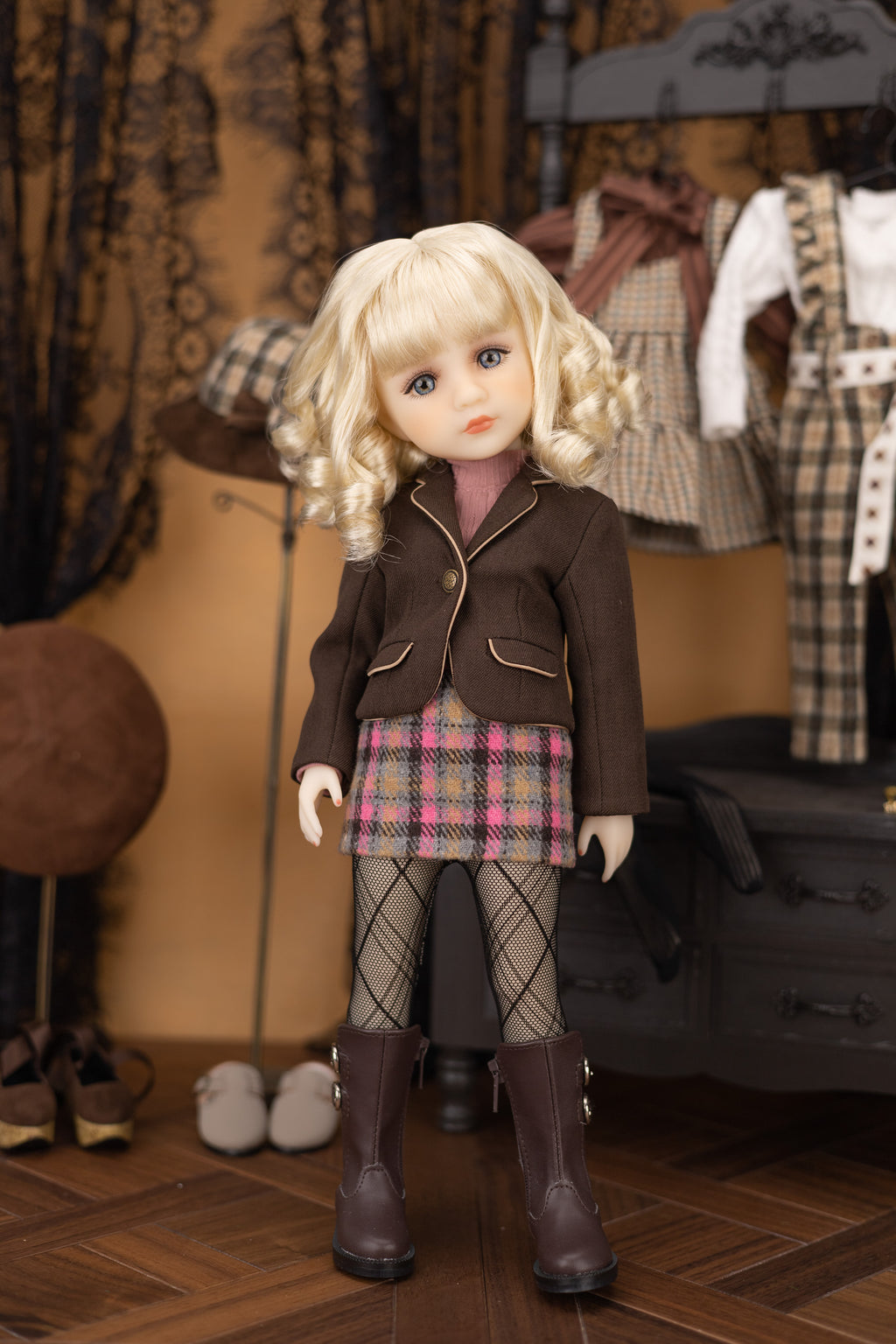 Doll in a brown jacket and plaid skirt standing in a room with clothing and shoes.