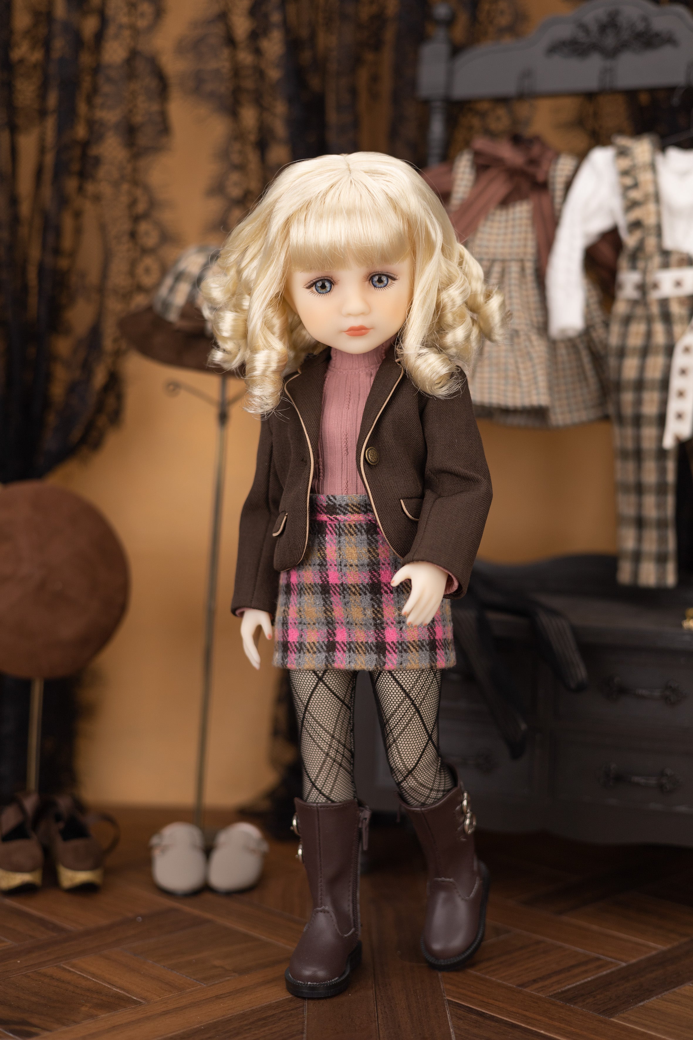 Doll in a plaid outfit with a brown jacket and boots, standing in a room with clothing and shoes.
