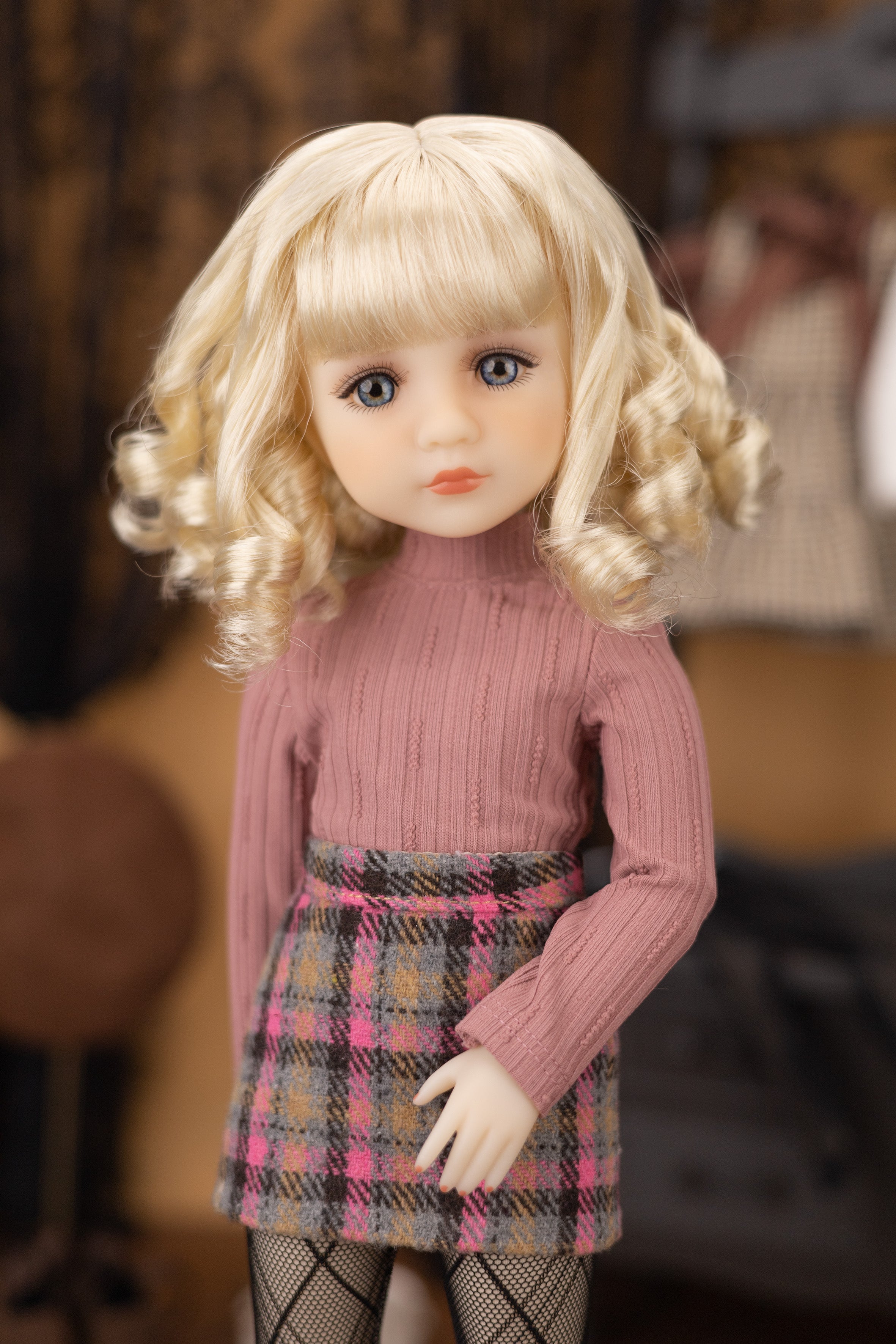 Doll with blonde hair and a pink sweater in a blurred indoor setting