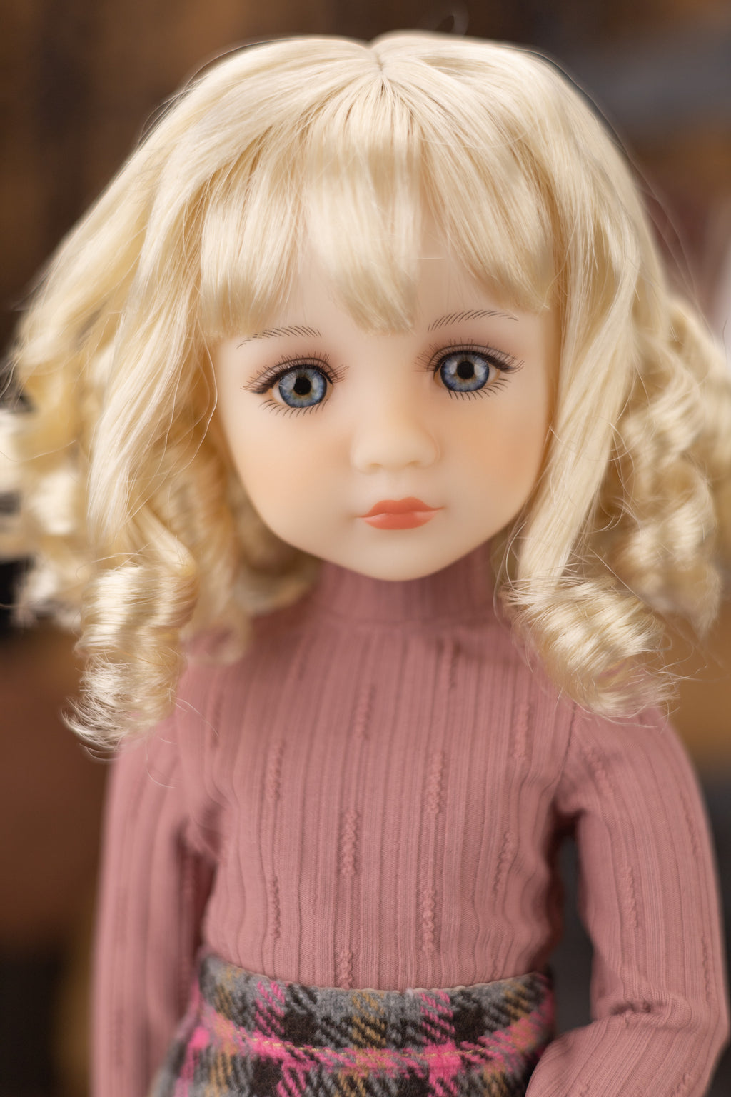 Doll with blonde hair and a pink sweater against a blurred background