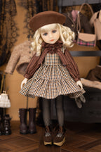 Doll in a vintage outfit with a checkered dress and brown beret, surrounded by vintage clothing.
