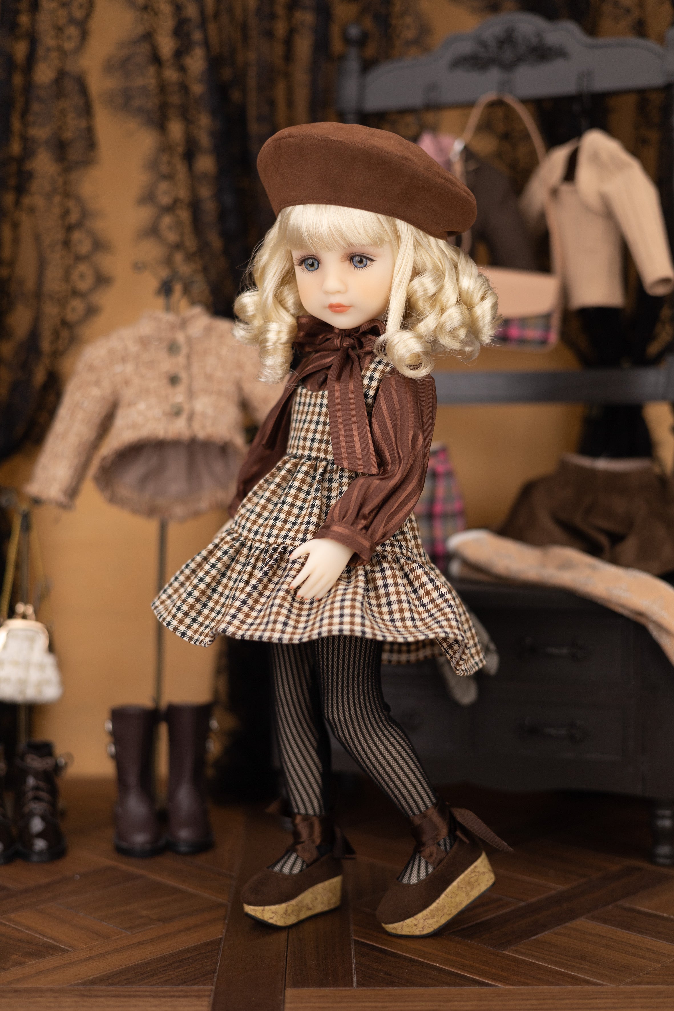 Doll in a checkered dress with a brown beret standing in a room with vintage clothing and furniture.