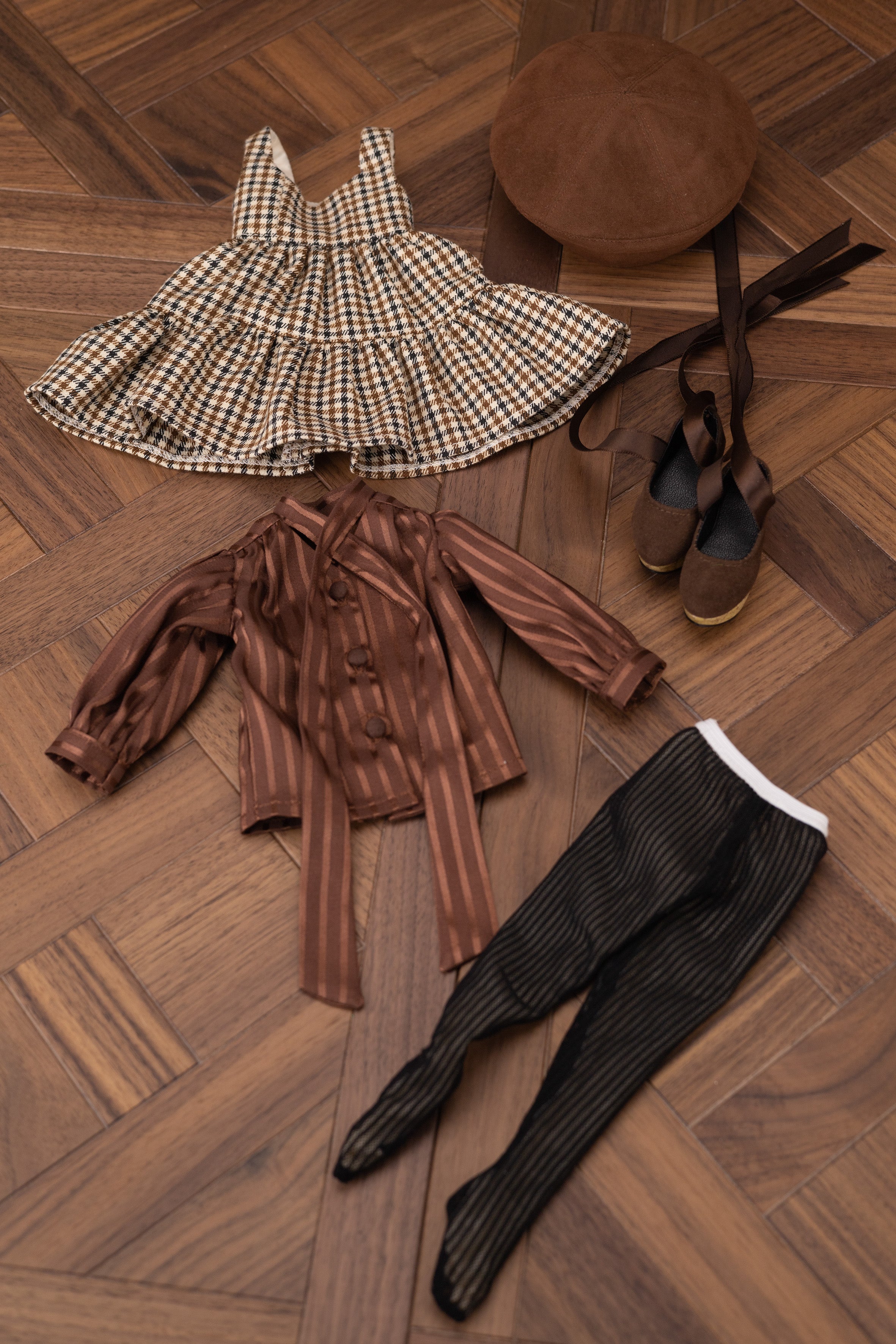 Children's clothing and accessories on a wooden floor including a dress, shirt, pants, shoes, and hat.