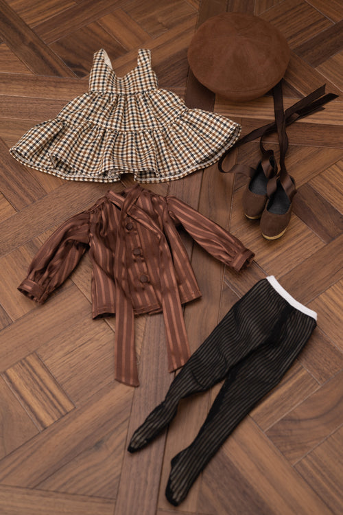 Children's clothing and accessories on a wooden floor including a dress, shirt, pants, shoes, and hat.