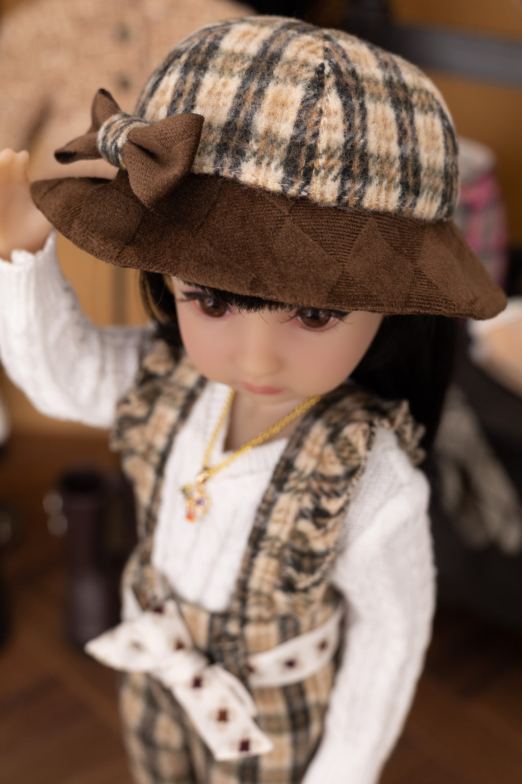 Doll wearing a plaid hat with a bow and formal outfit.