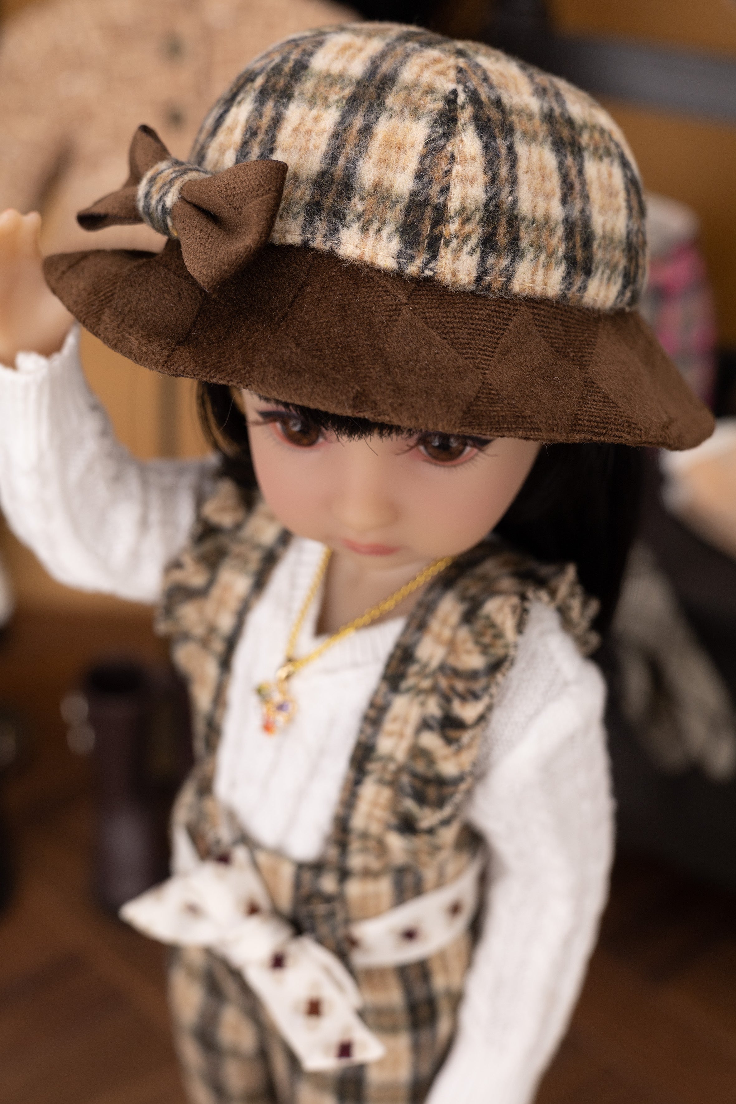Doll wearing a plaid hat with a bow and formal outfit.