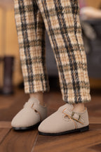 Beige shoes with gold buckles worn with plaid pants on a wooden floor.