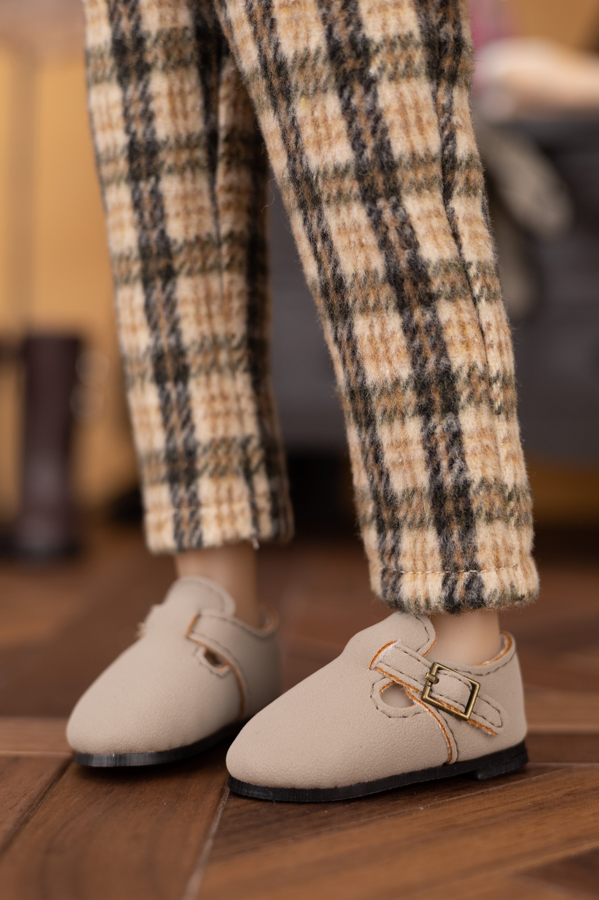 Beige shoes with gold buckles worn with plaid pants on a wooden floor.