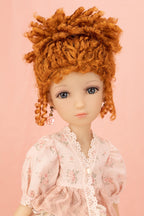A close-up of a doll with curly orange-red hair, blue eyes, and a pale pink floral dress against a solid pink background.