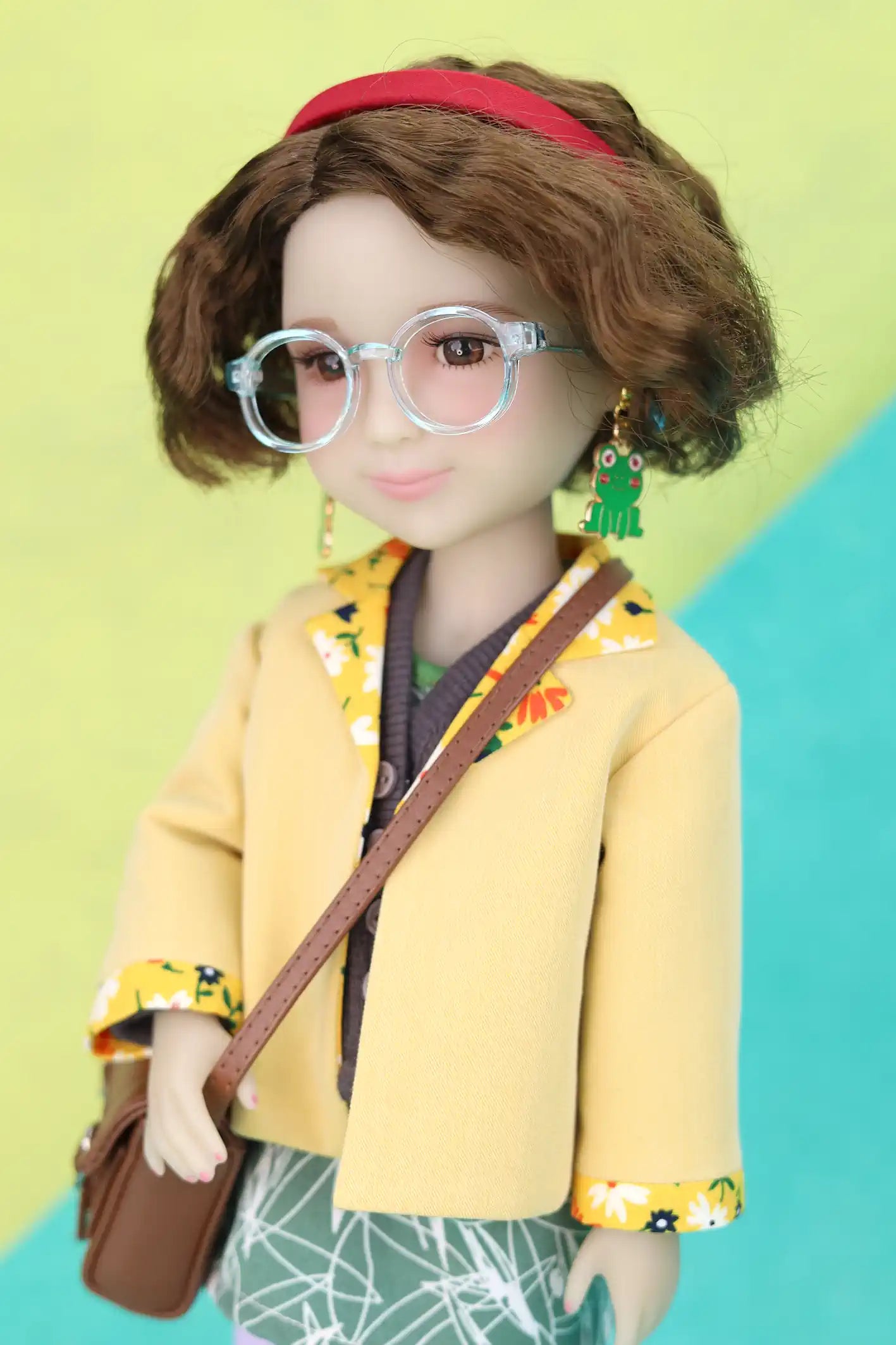 Ava wearing a yellow outfit with a red headband and glasses, standing against a colorful background.