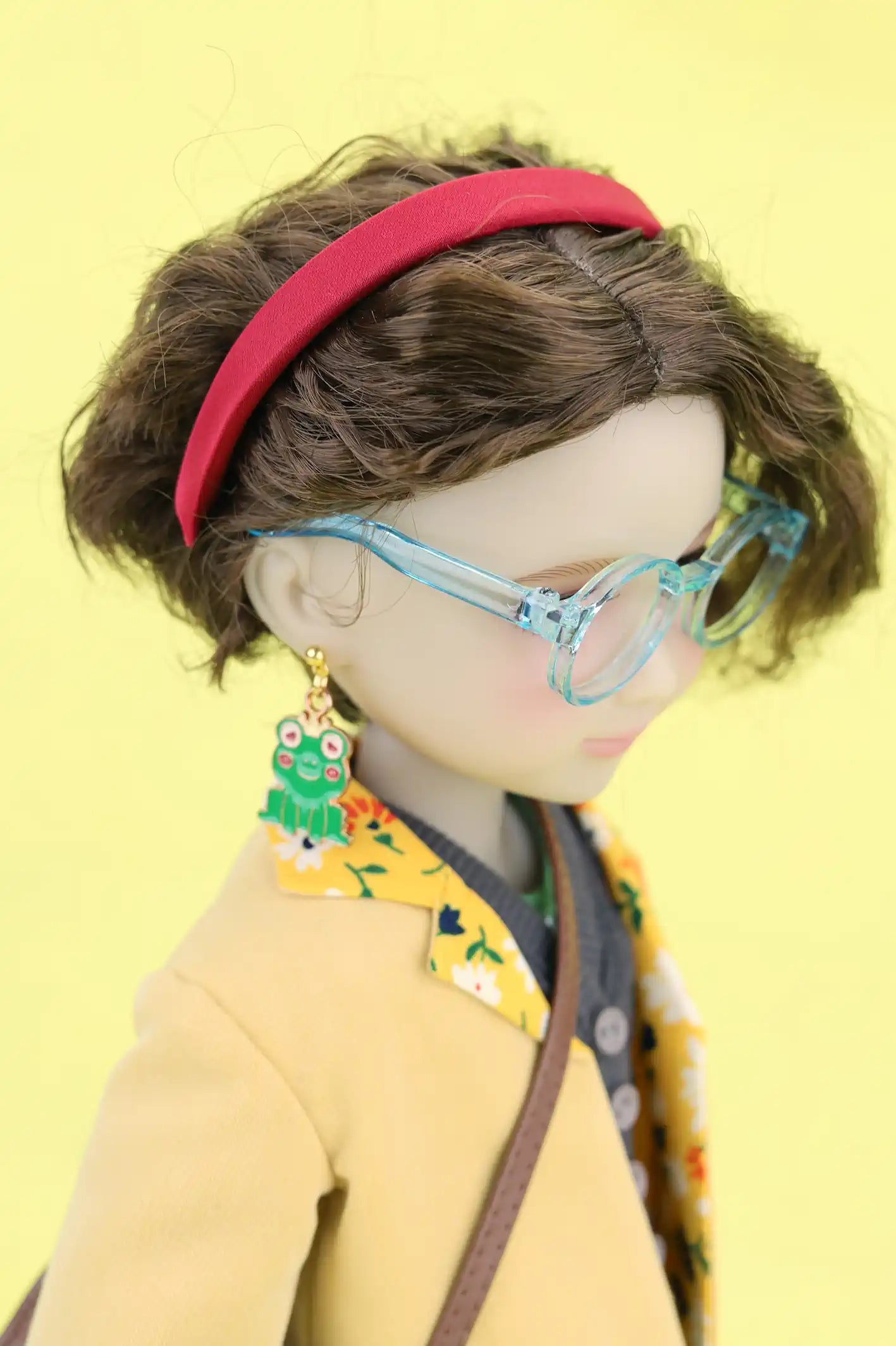 Ava wearing a red headband, blue glasses, and colorful earrings on a yellow background