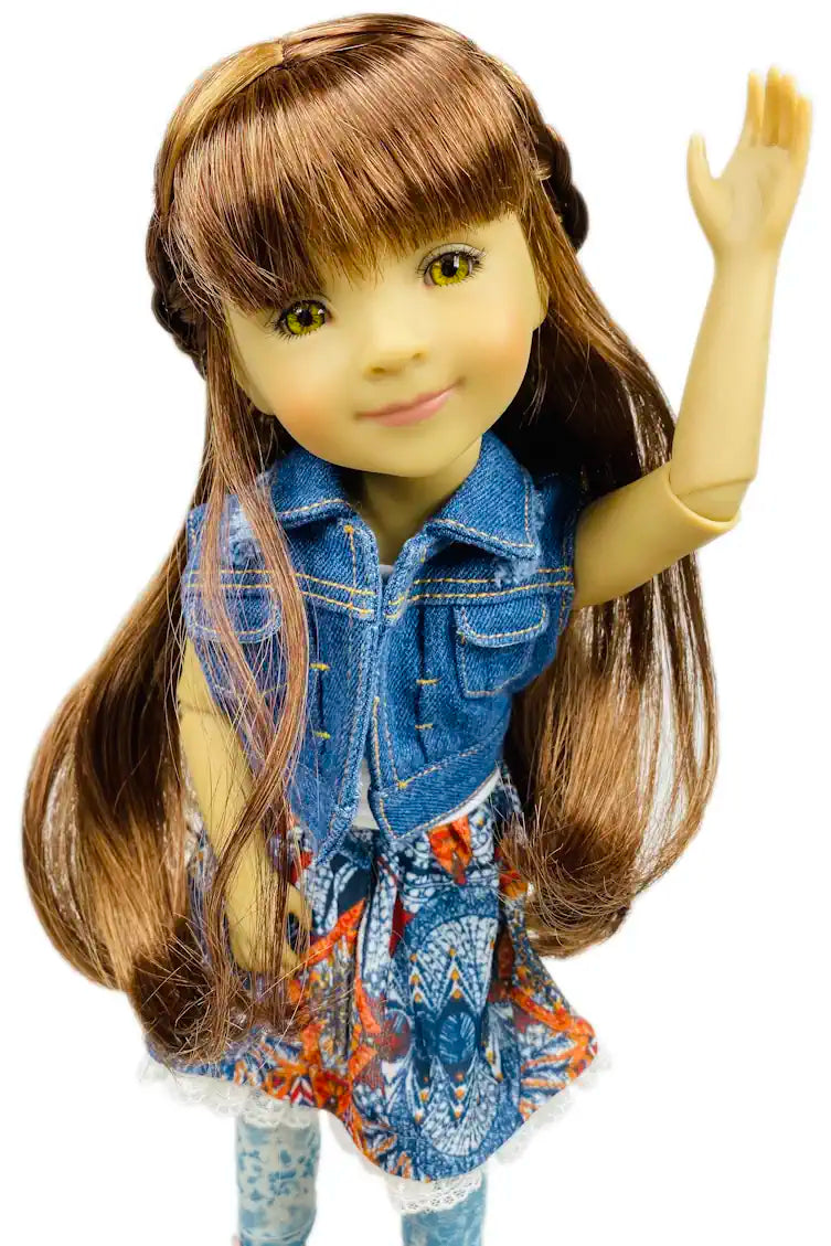 Bella with long brown hair wearing a denim vest over a colorful shirt on a white background