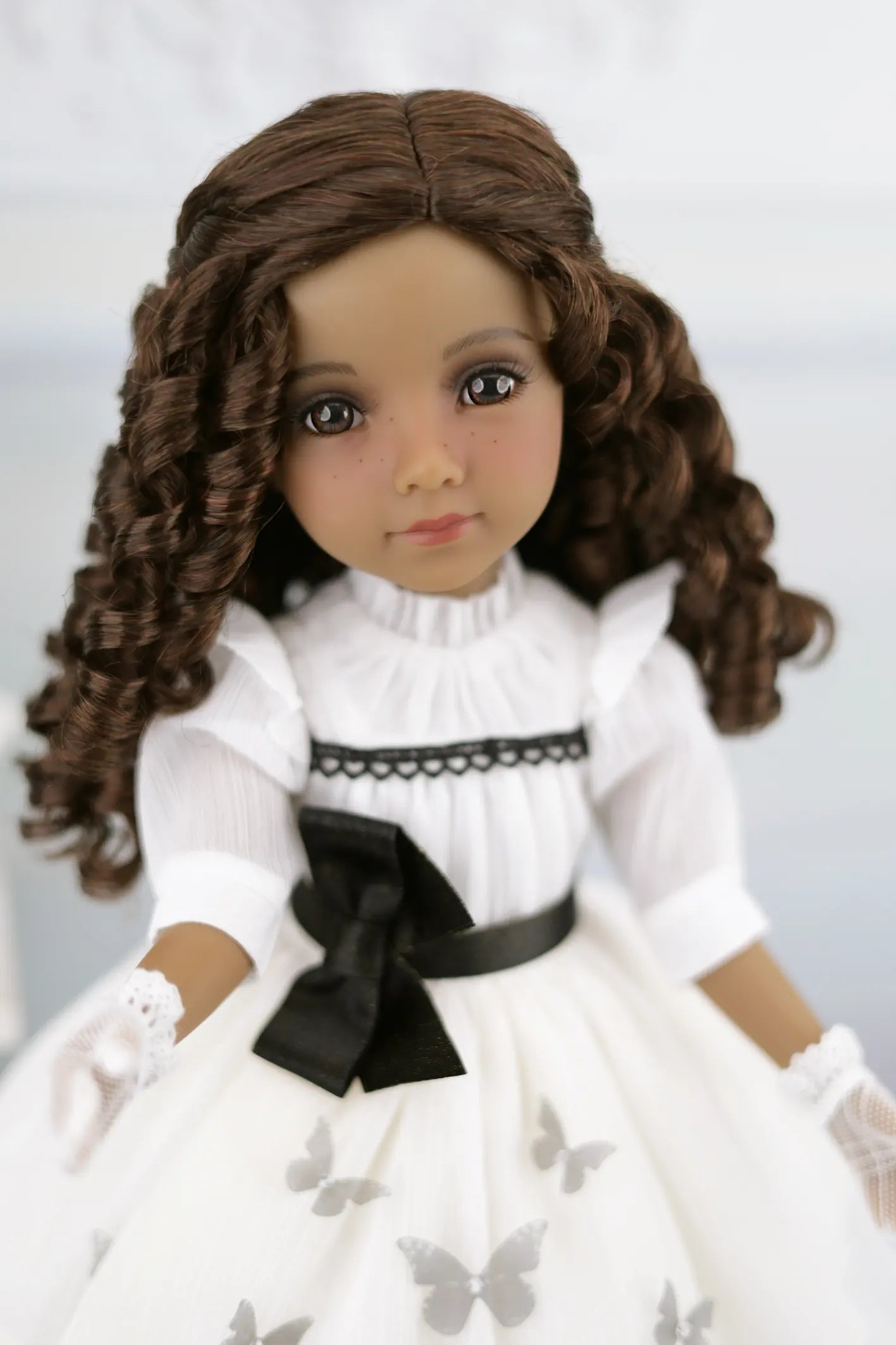 Esther wearing a white dress with a black bow and butterfly details on a plain background