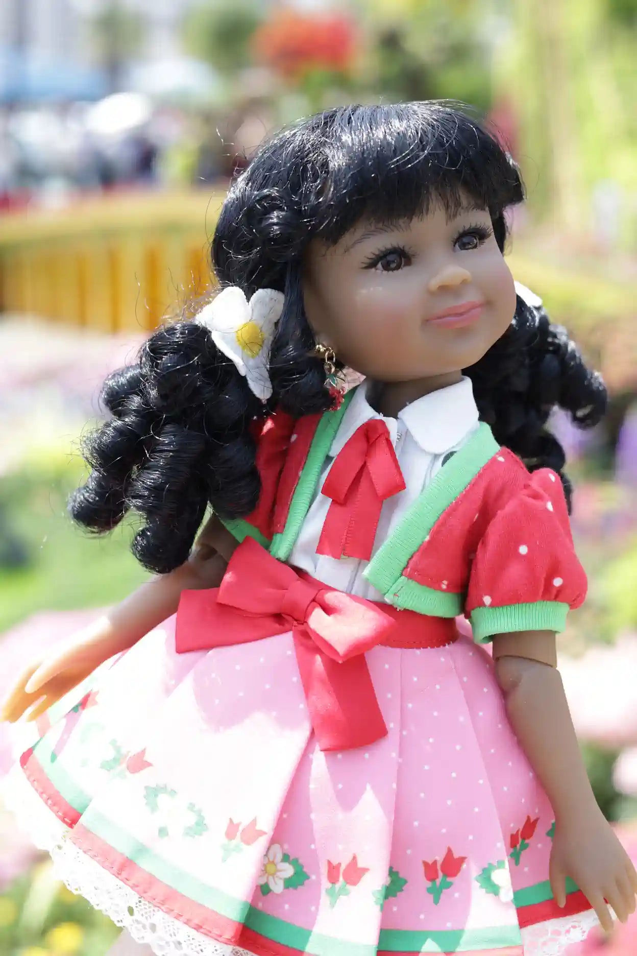 Kyra with black hair styled in pigtails, wearing a red and pink dress with green accents.