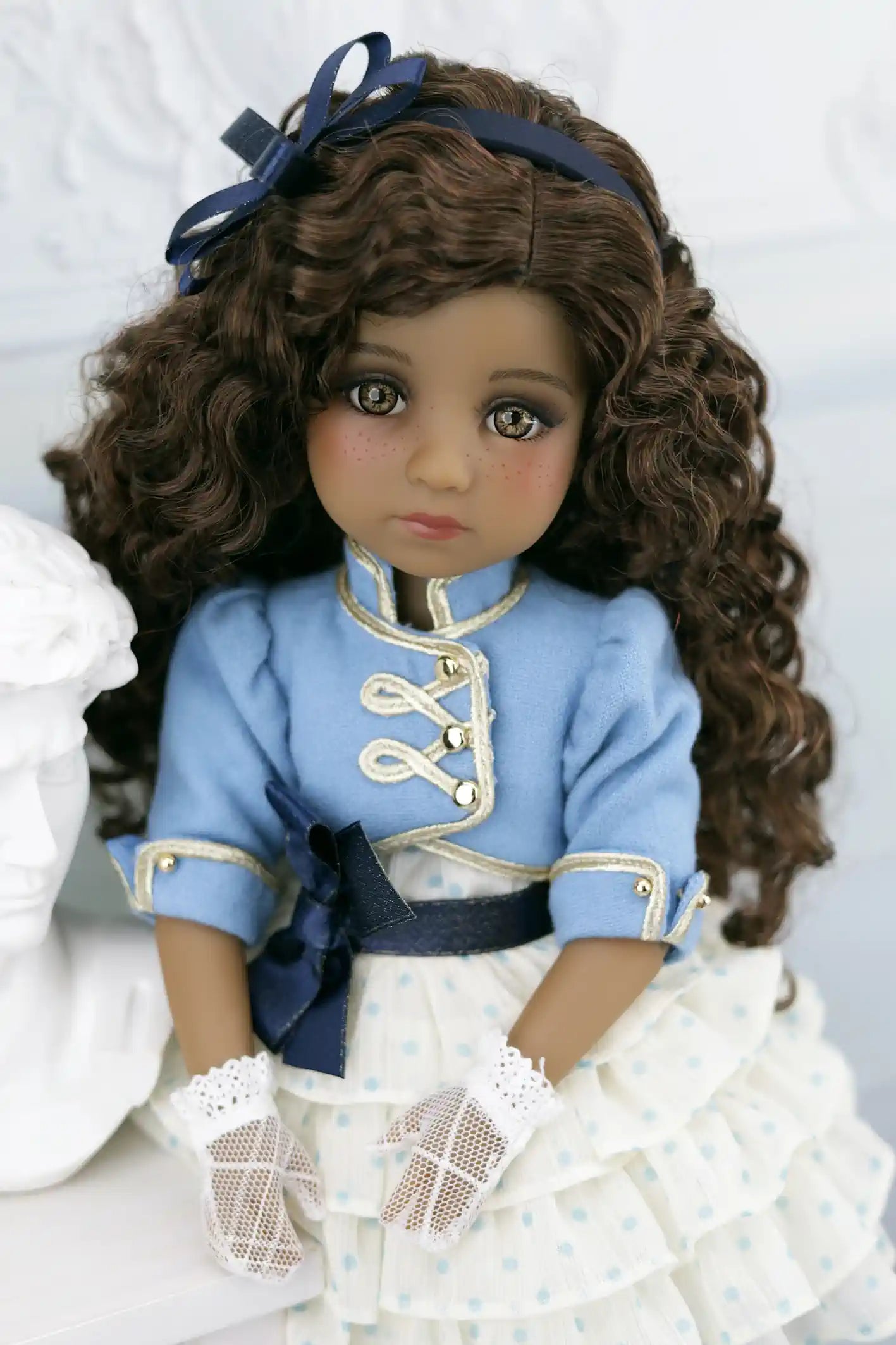 Ruth in a blue and white outfit with a bow on a white background