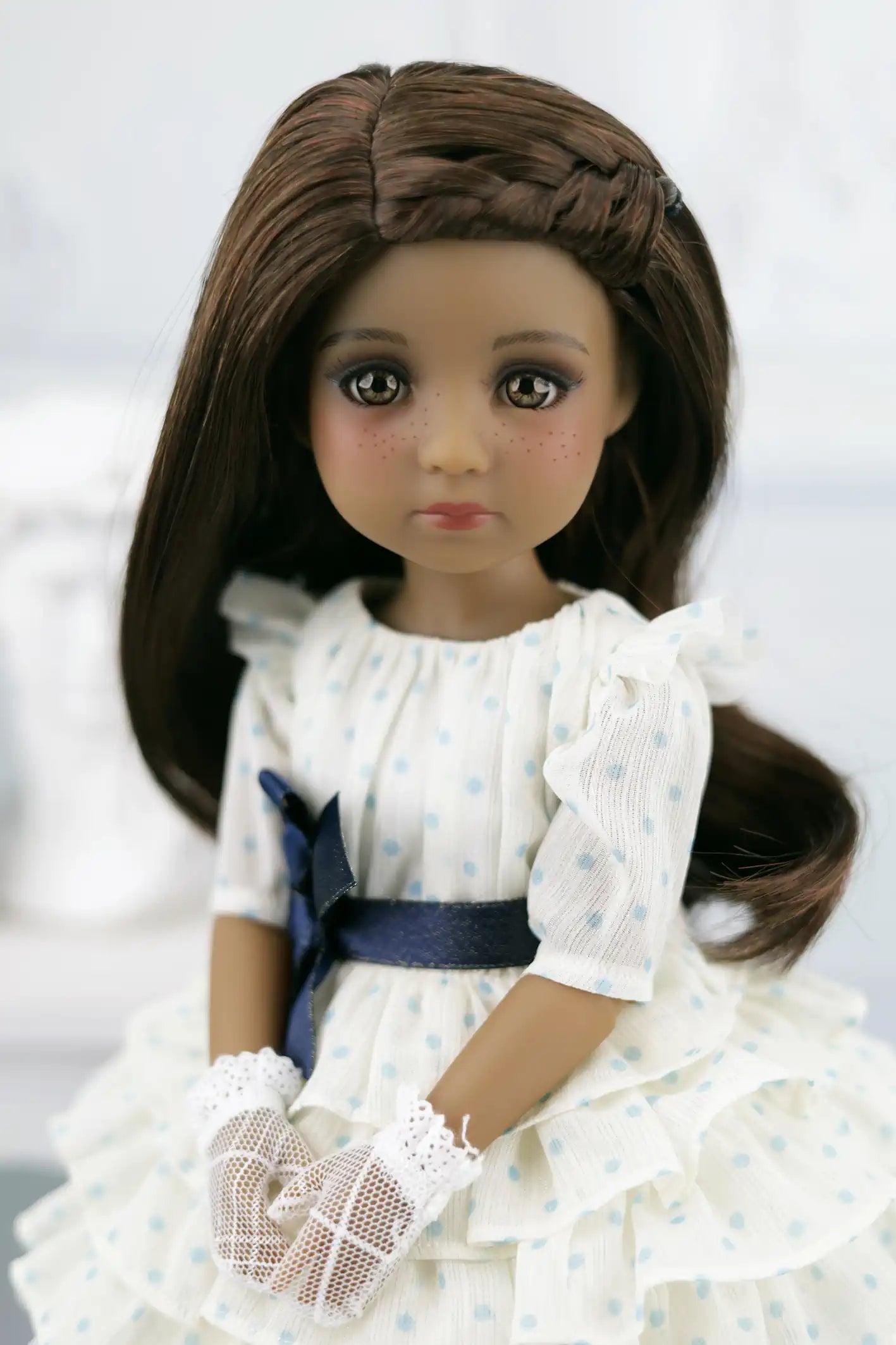 Ruth with long brown hair wearing a white dress with blue accents on a white background