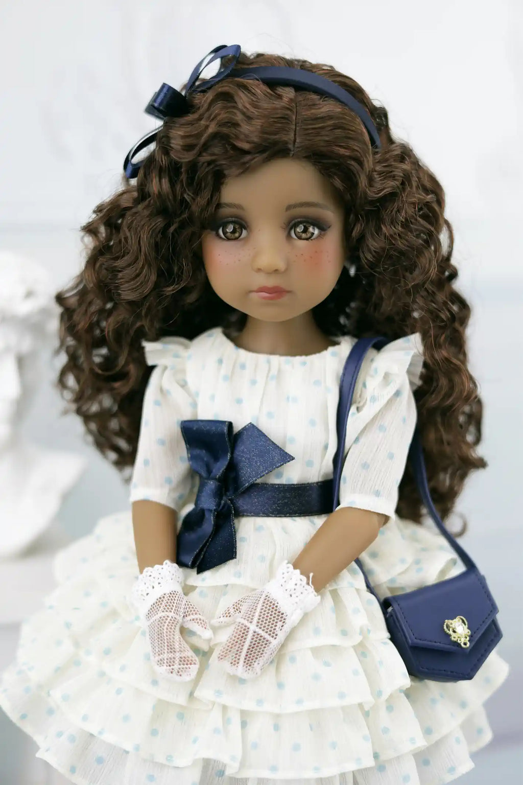 Ruth with curly hair wearing a white dress with blue accents and a blue handbag.