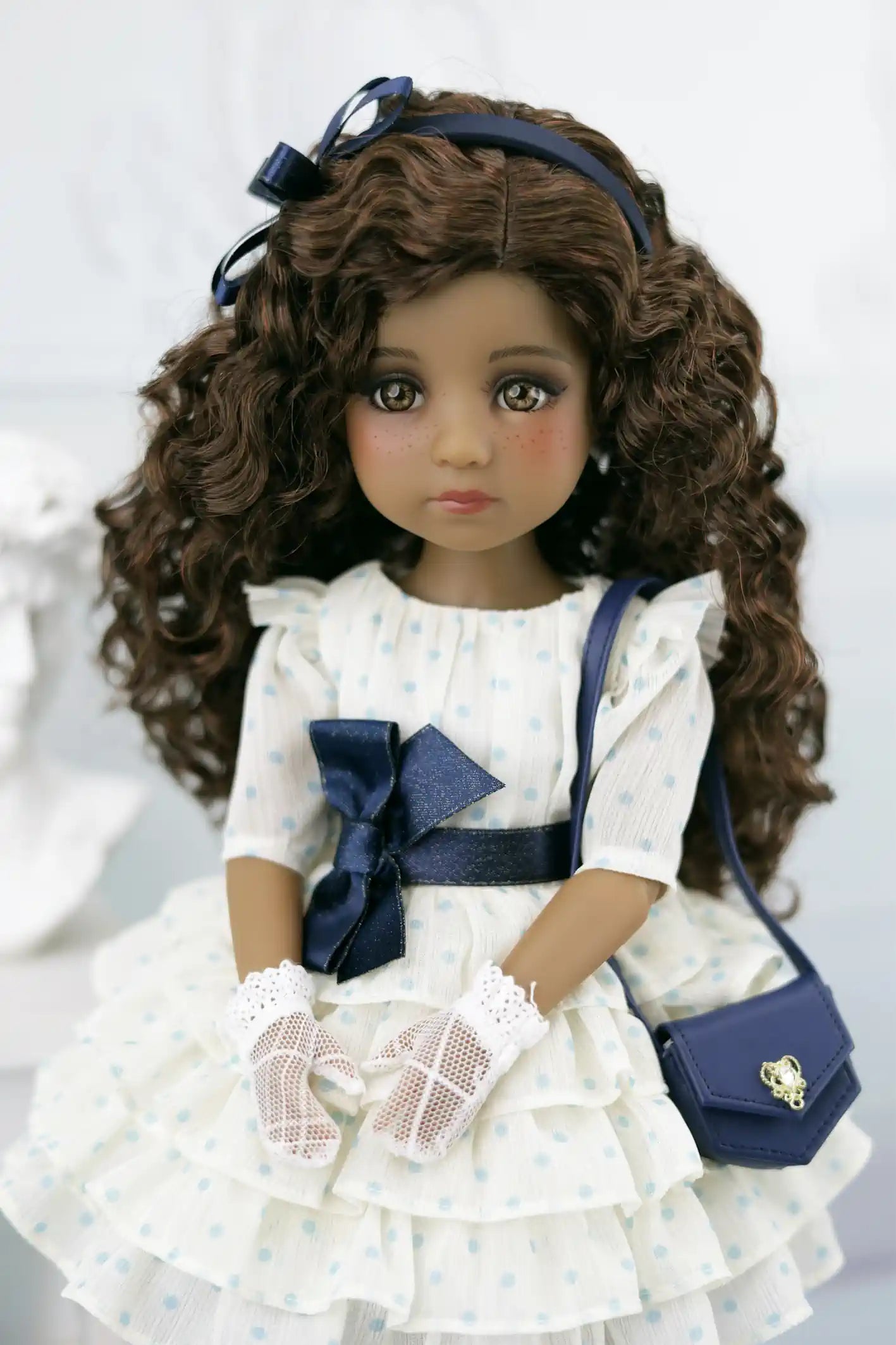 Ruth with curly hair wearing a white dress with blue accents and a blue handbag.