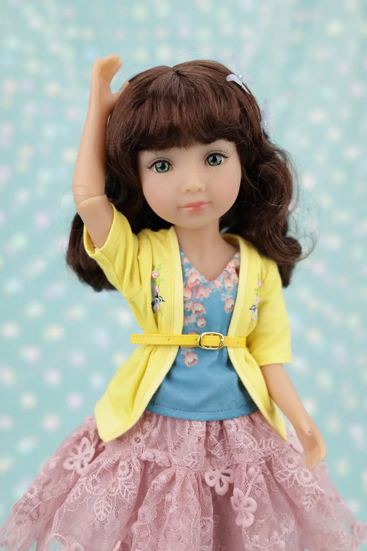 Juniper wearing a yellow cardigan, blue top, and pink skirt against a light blue background with polka dots.