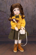 Doll in a yellow coat with a teddy bear and basket against a textured wall.
