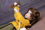 Doll in a yellow coat holding a smaller doll against a textured wall background