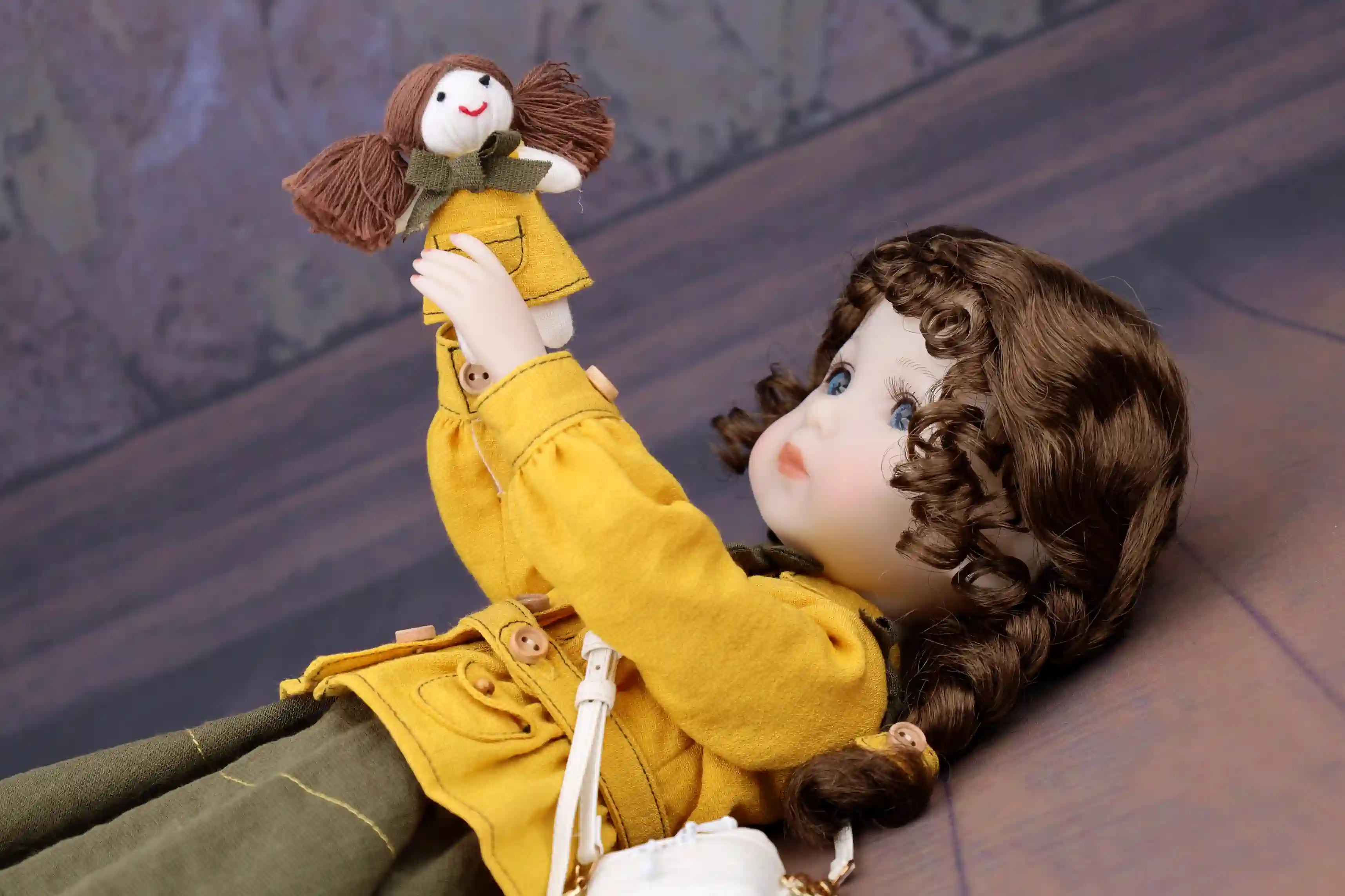 Doll in a yellow coat holding a smaller doll against a textured wall background