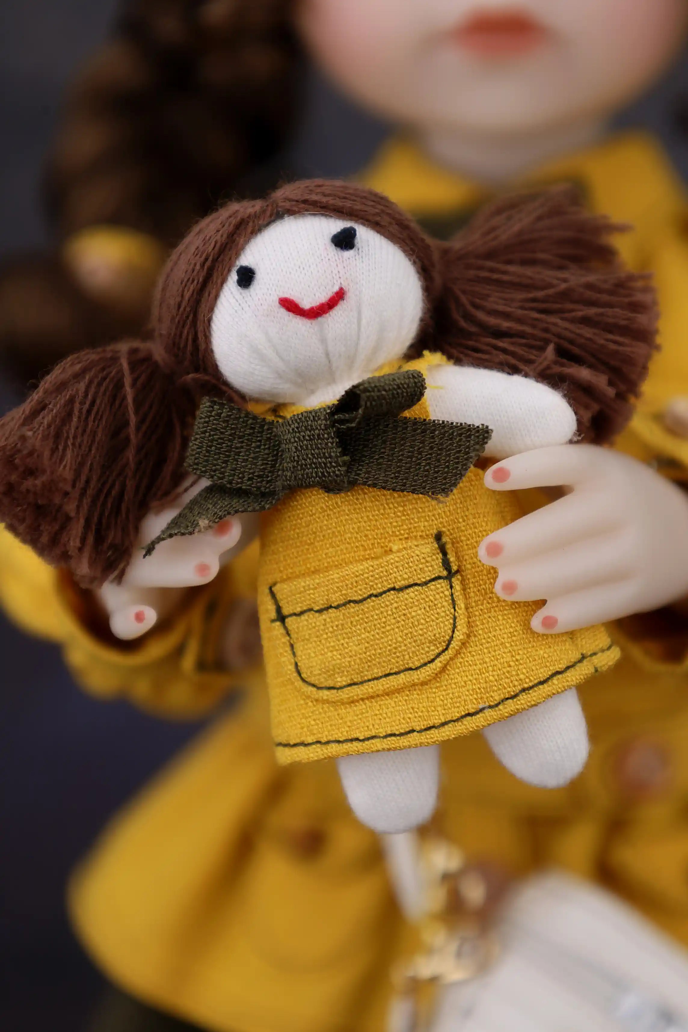 Small doll with brown hair and a yellow dress holding a green bow.