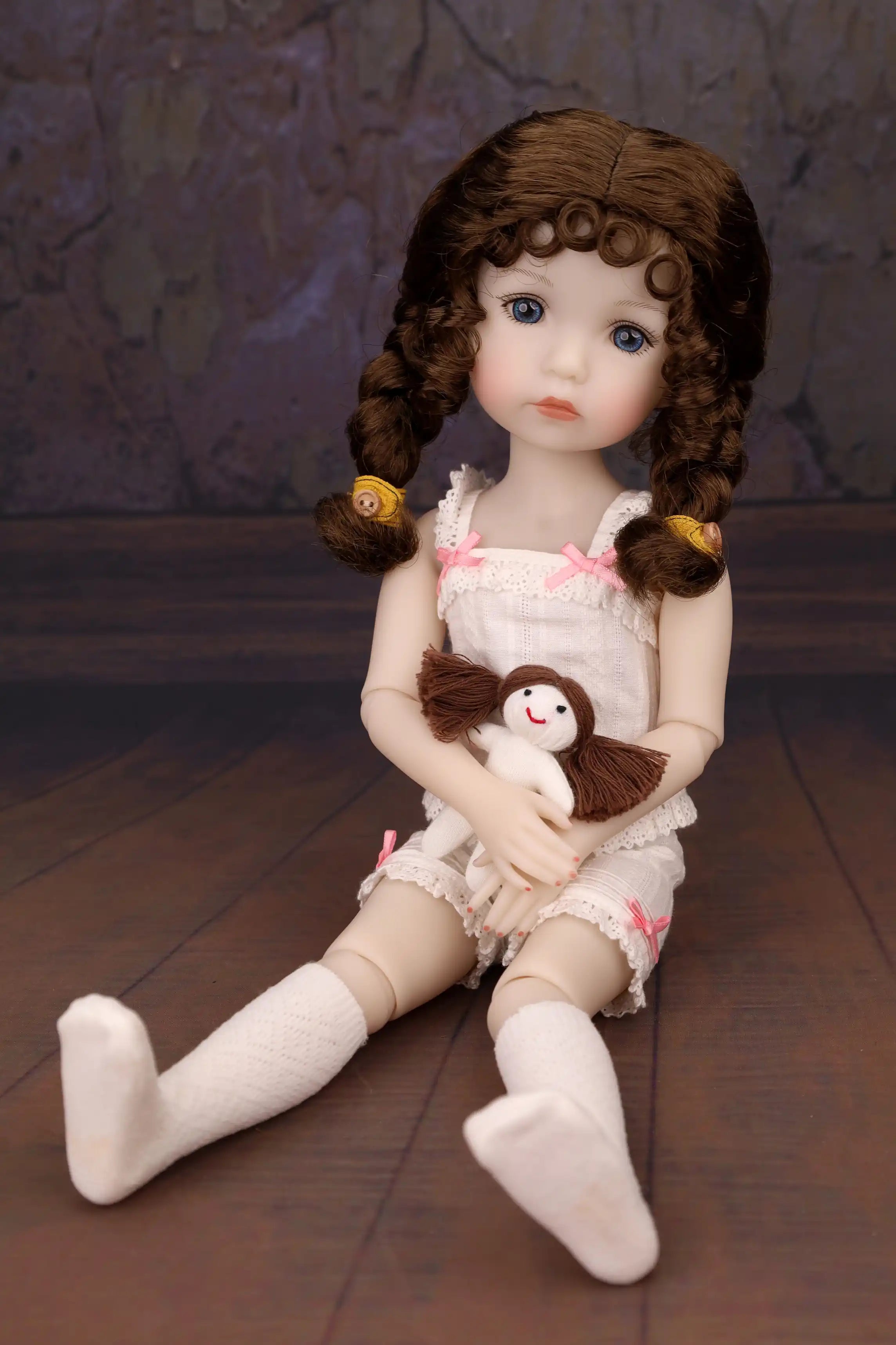 Doll with braided hair holding a small plush toy on a wooden floor.