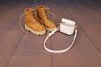 Pair of brown boots with a white handbag on a wooden floor.