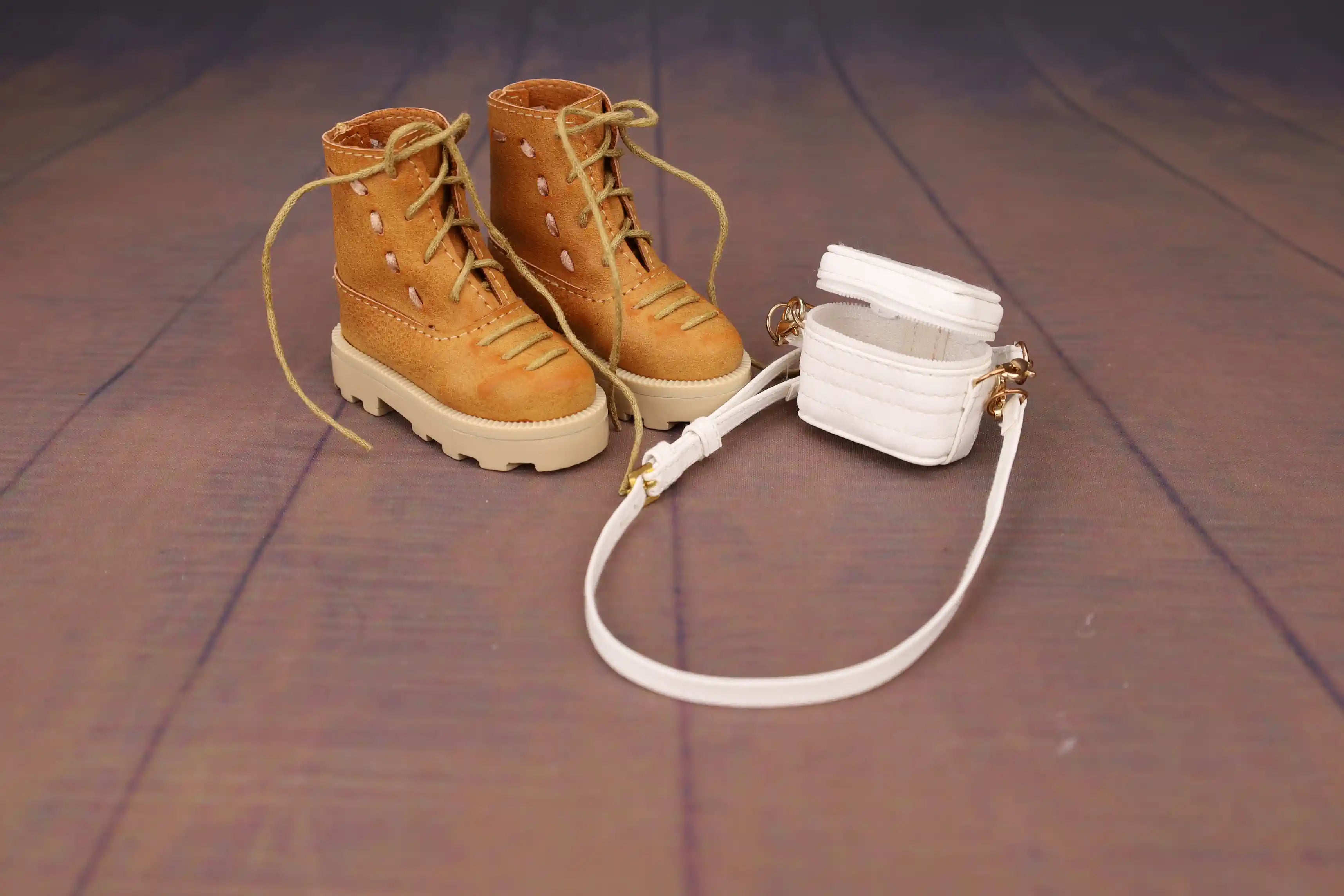Pair of brown boots with a white handbag on a wooden floor.