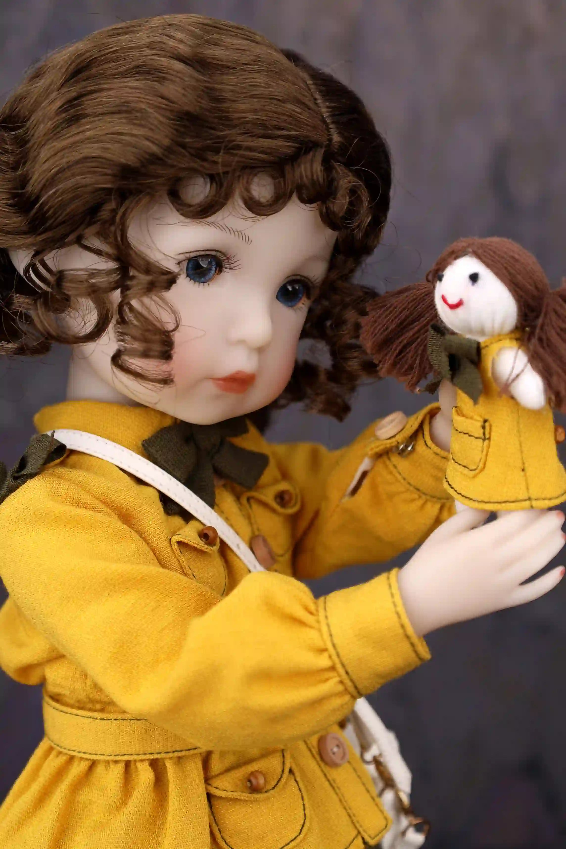 Doll in a yellow coat holding a smaller doll with brown hair against a dark background