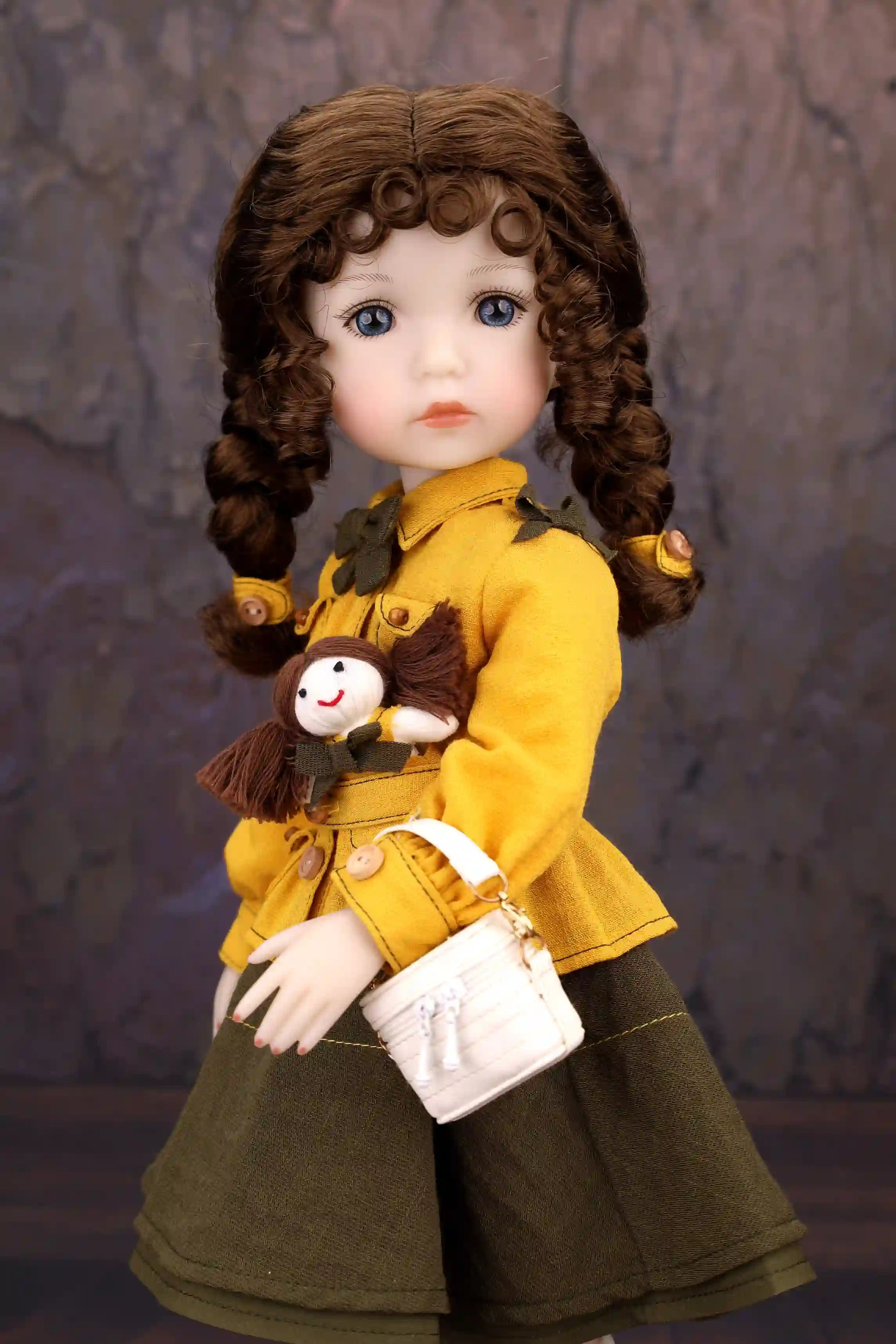 Doll wearing a yellow coat with a small monkey plush toy, against a textured gray background.