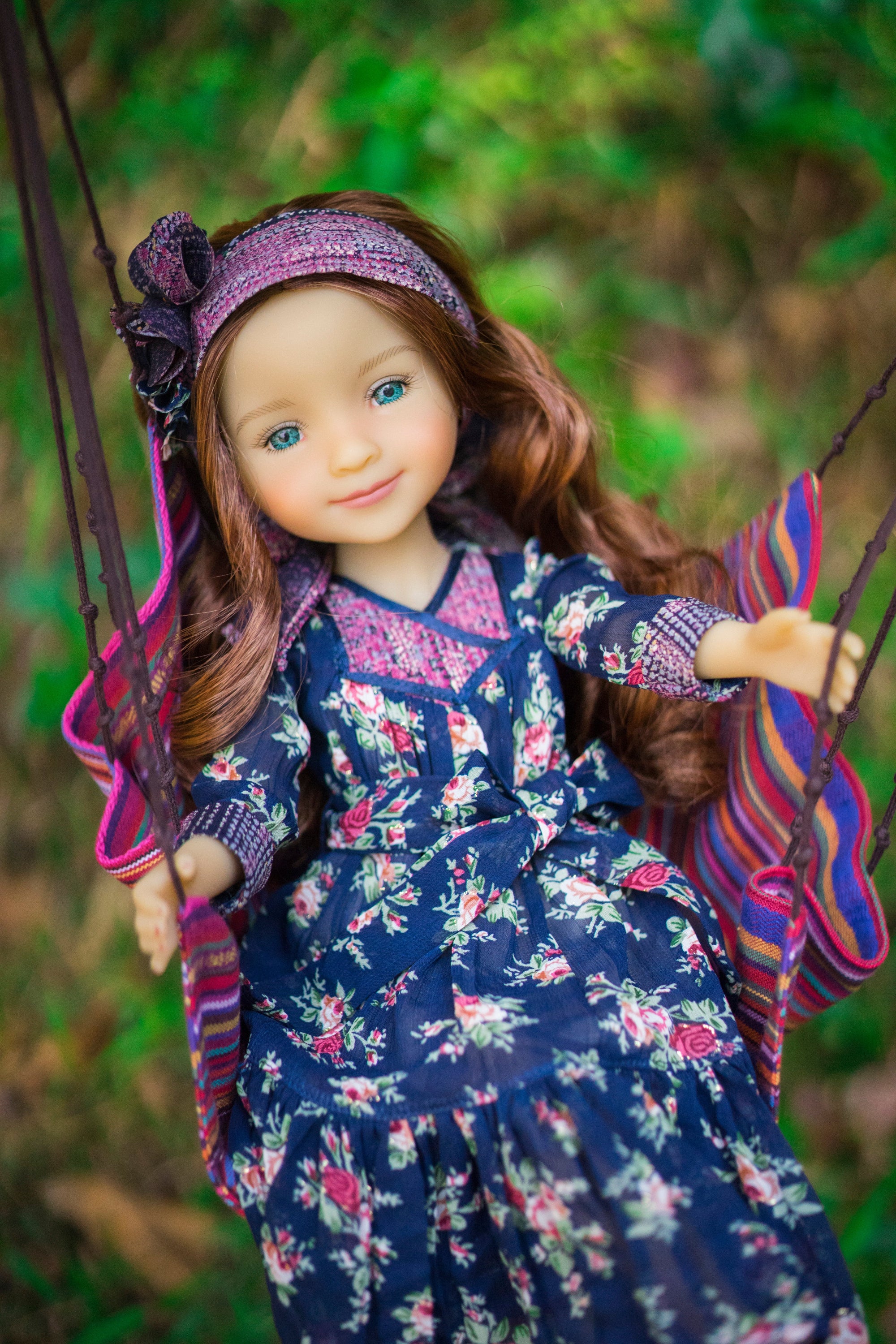 Doll in a floral dress on a swing with a blurred natural background