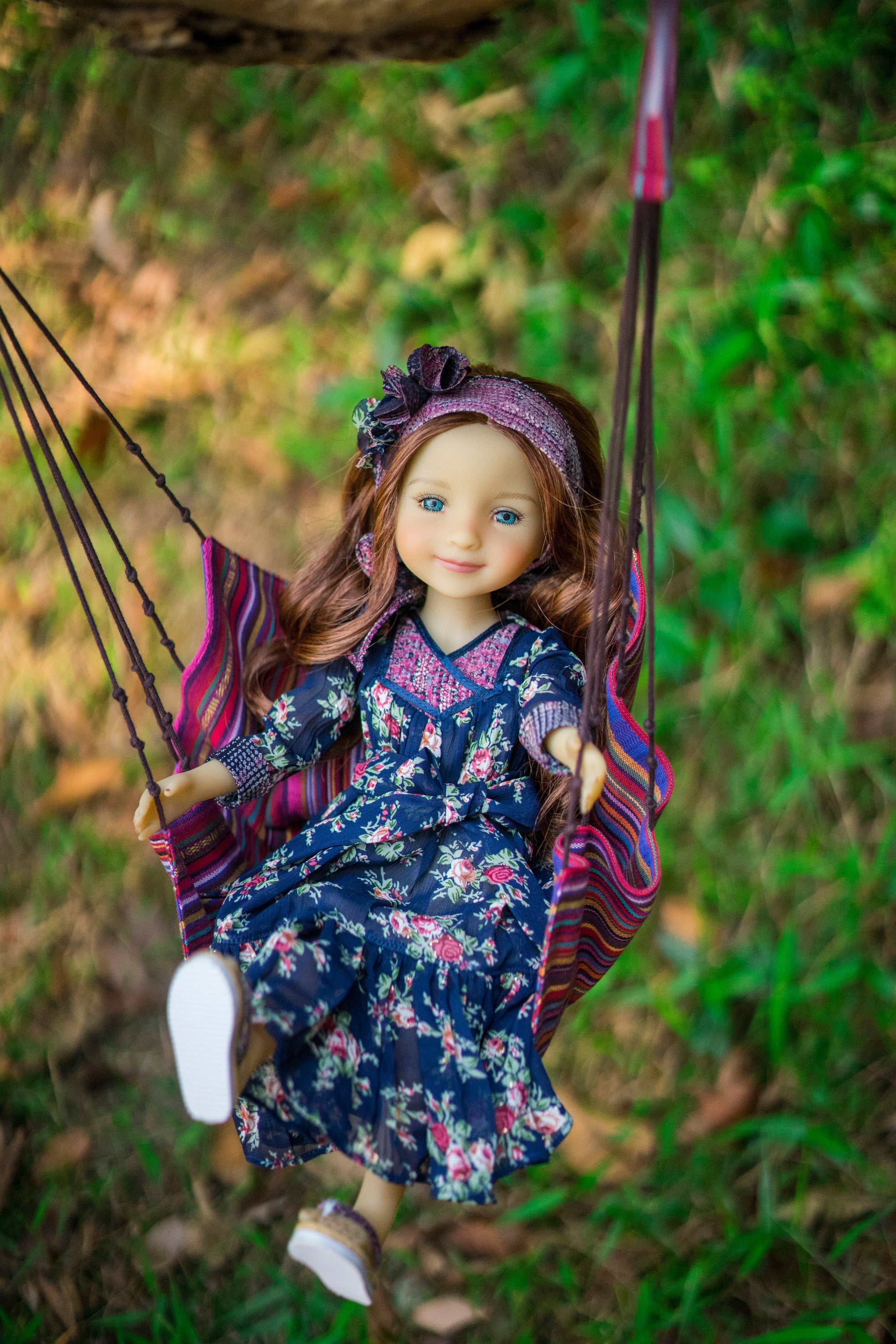 Doll in a floral dress and headscarf sitting in a swing with a natural background