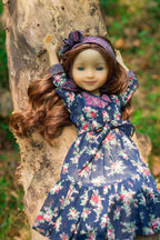 Doll in a floral dress standing against a tree trunk outdoors