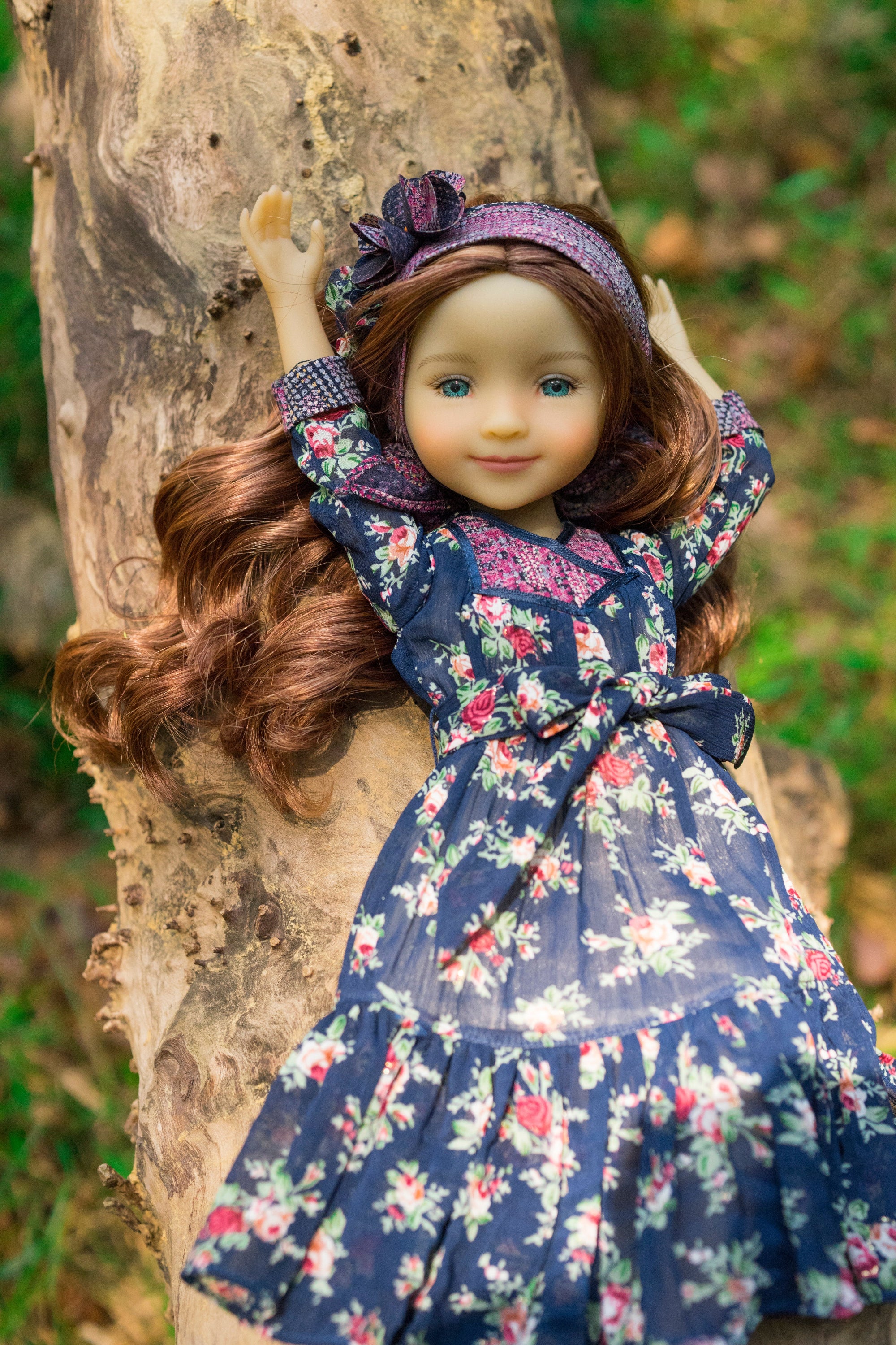 Doll in a floral dress standing against a tree trunk outdoors