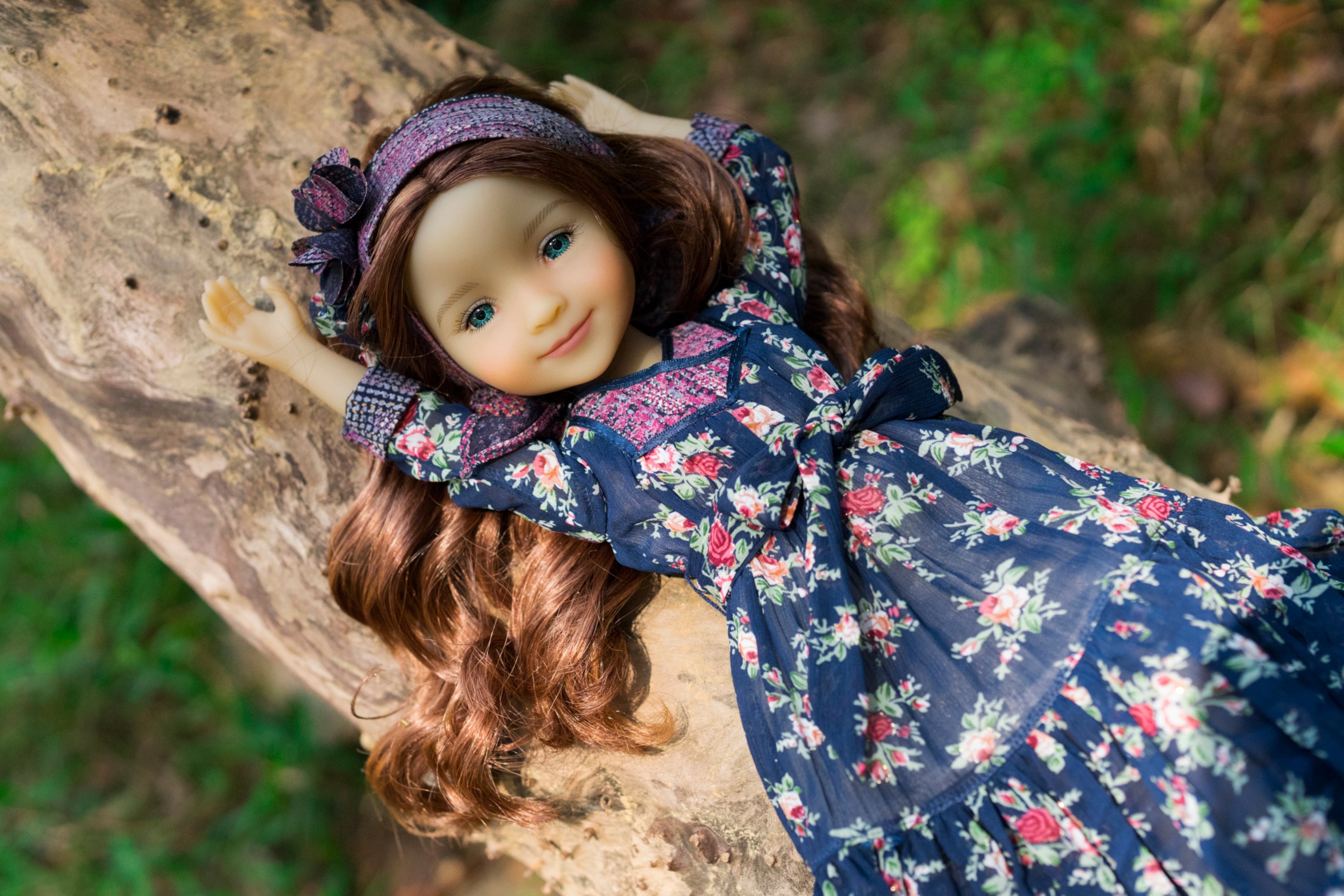 Doll in a floral dress and headband lying on a tree branch with a natural background