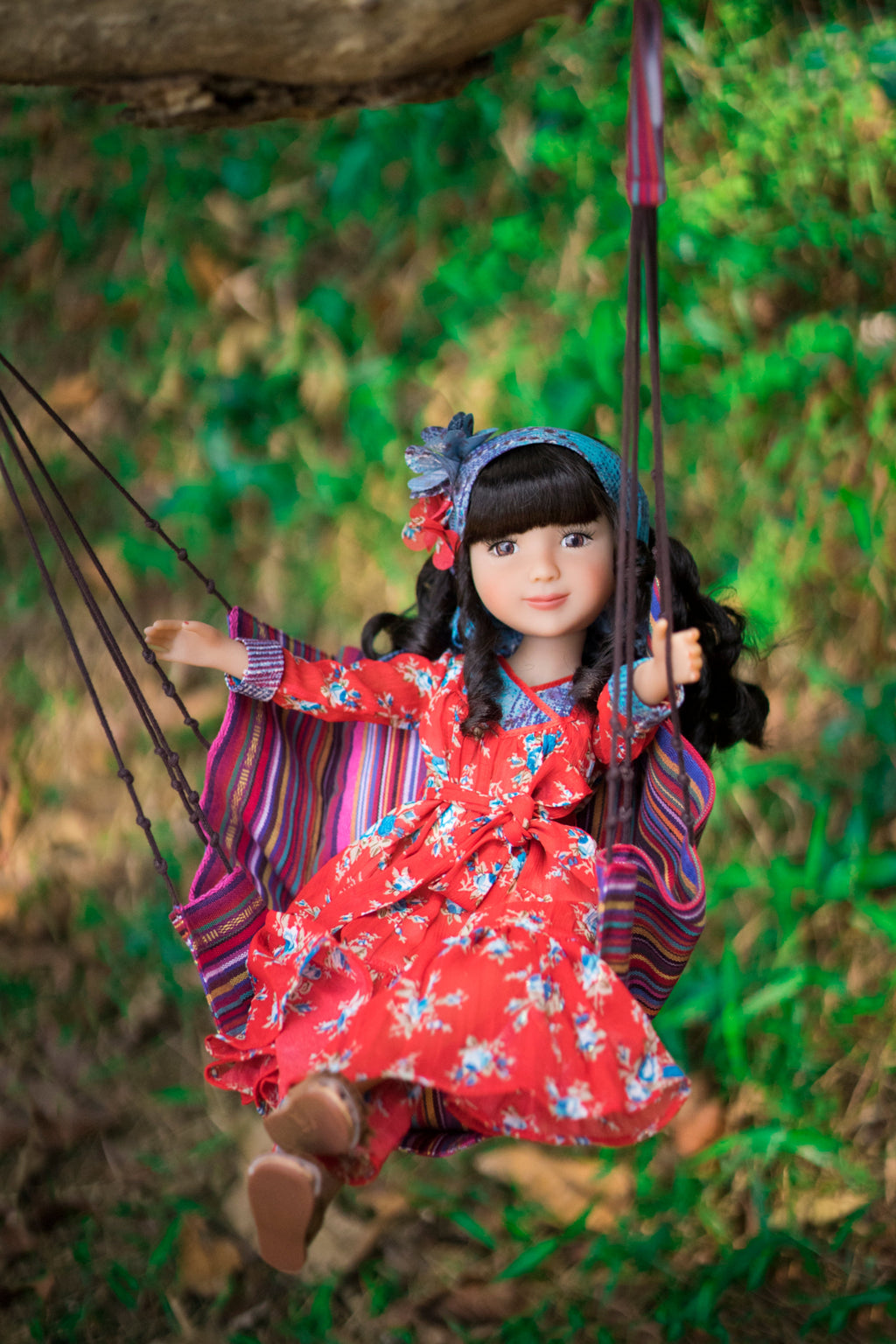 Doll in a red floral dress on a swing with a natural background