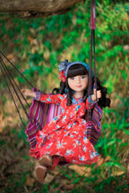 Doll in a red floral dress on a swing with a natural background